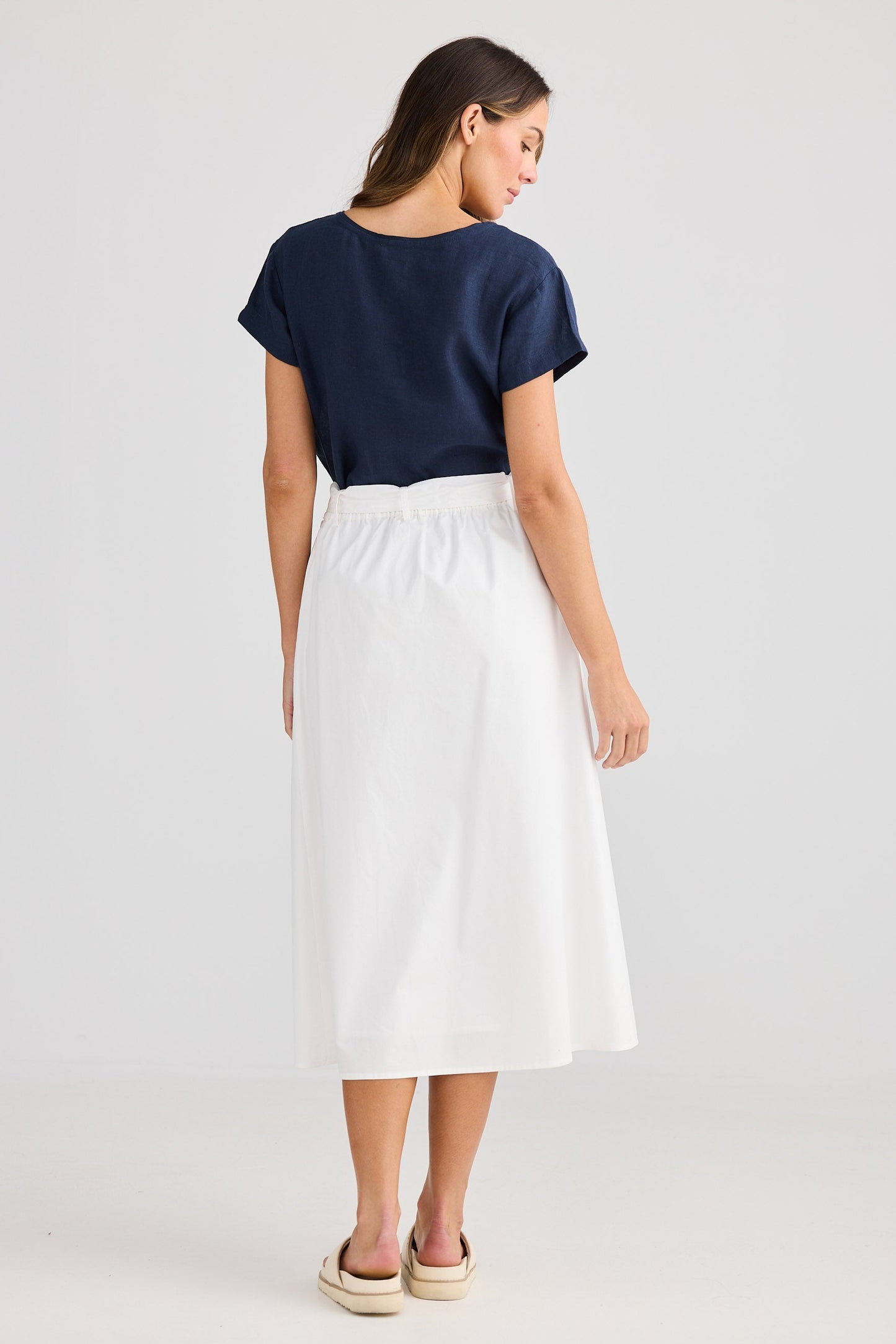 Woman wearing a navy top and white skirt on a light gray background