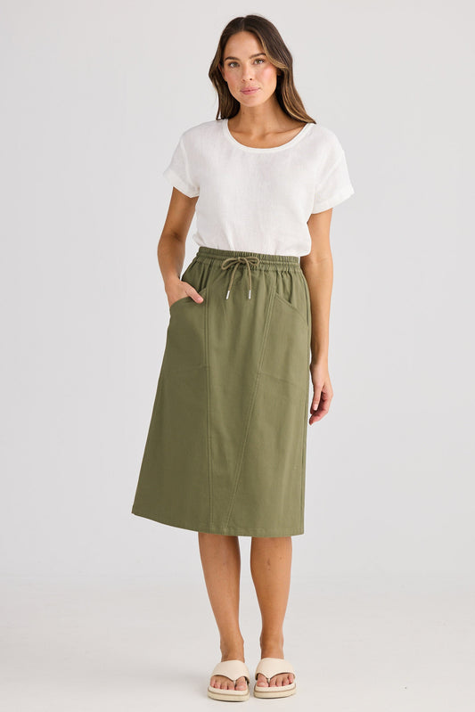 Woman wearing a white top and green skirt on a plain background