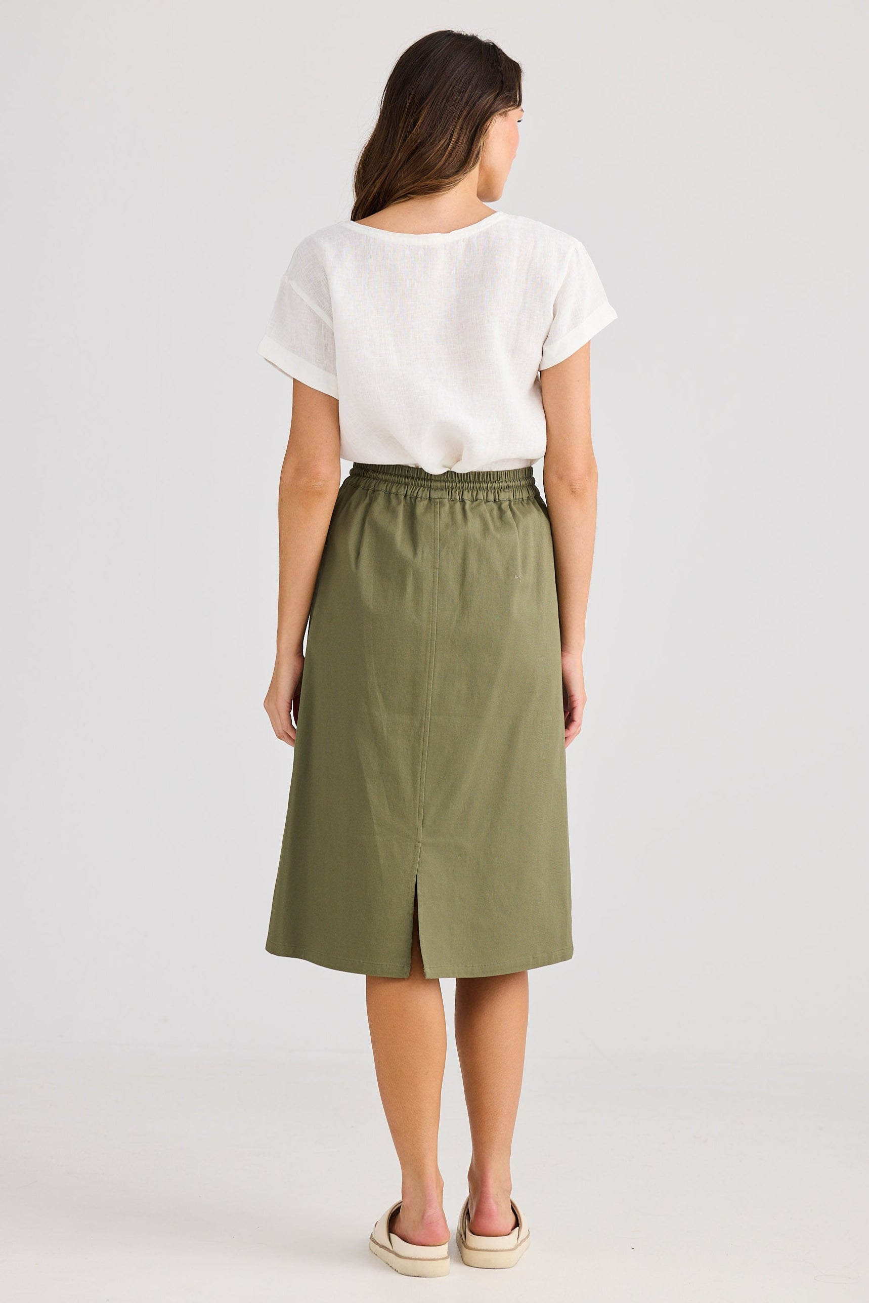 Woman wearing a white top and green skirt on a plain background