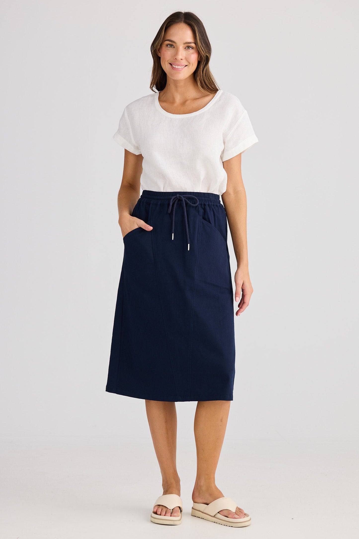 Woman wearing a navy skirt and white top on a light gray background