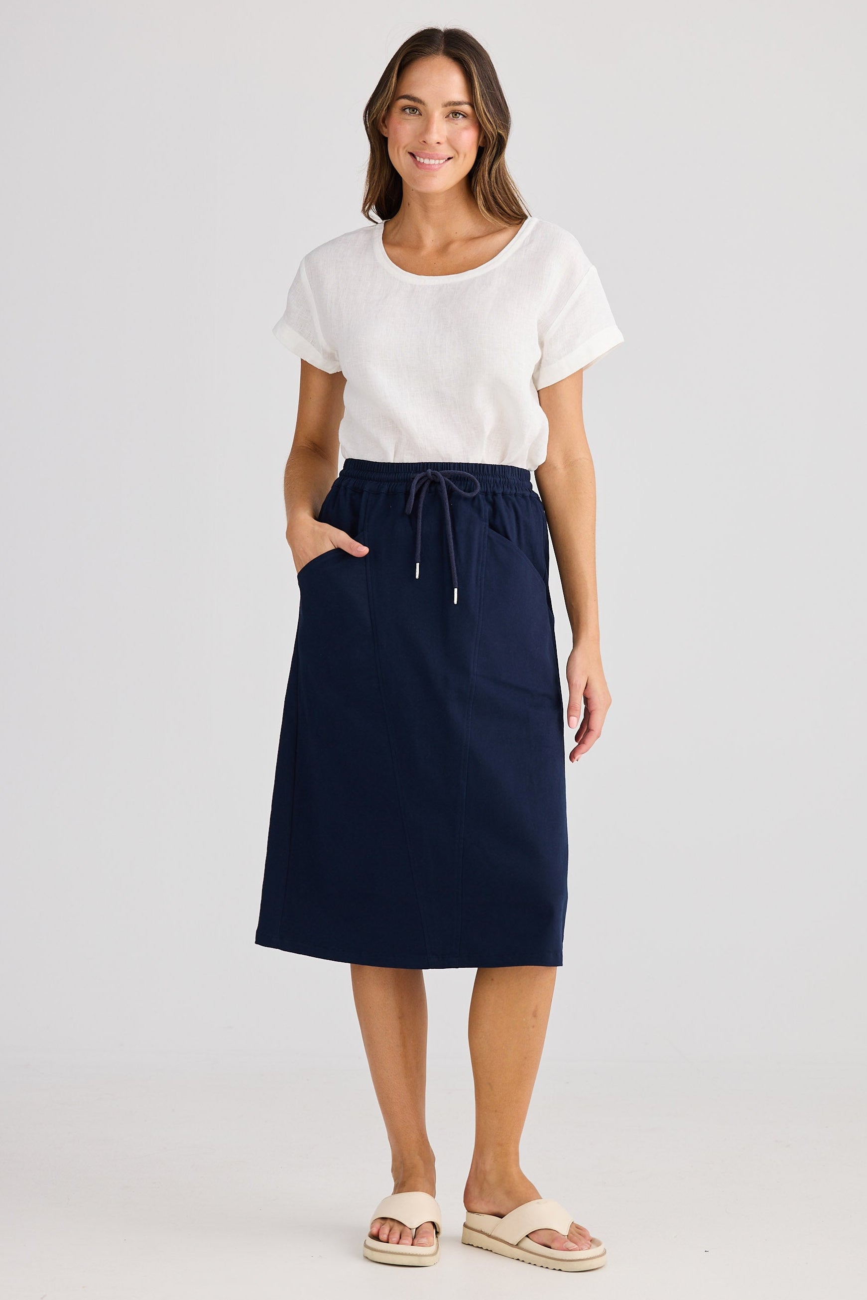 Woman wearing a navy skirt and white top on a light gray background