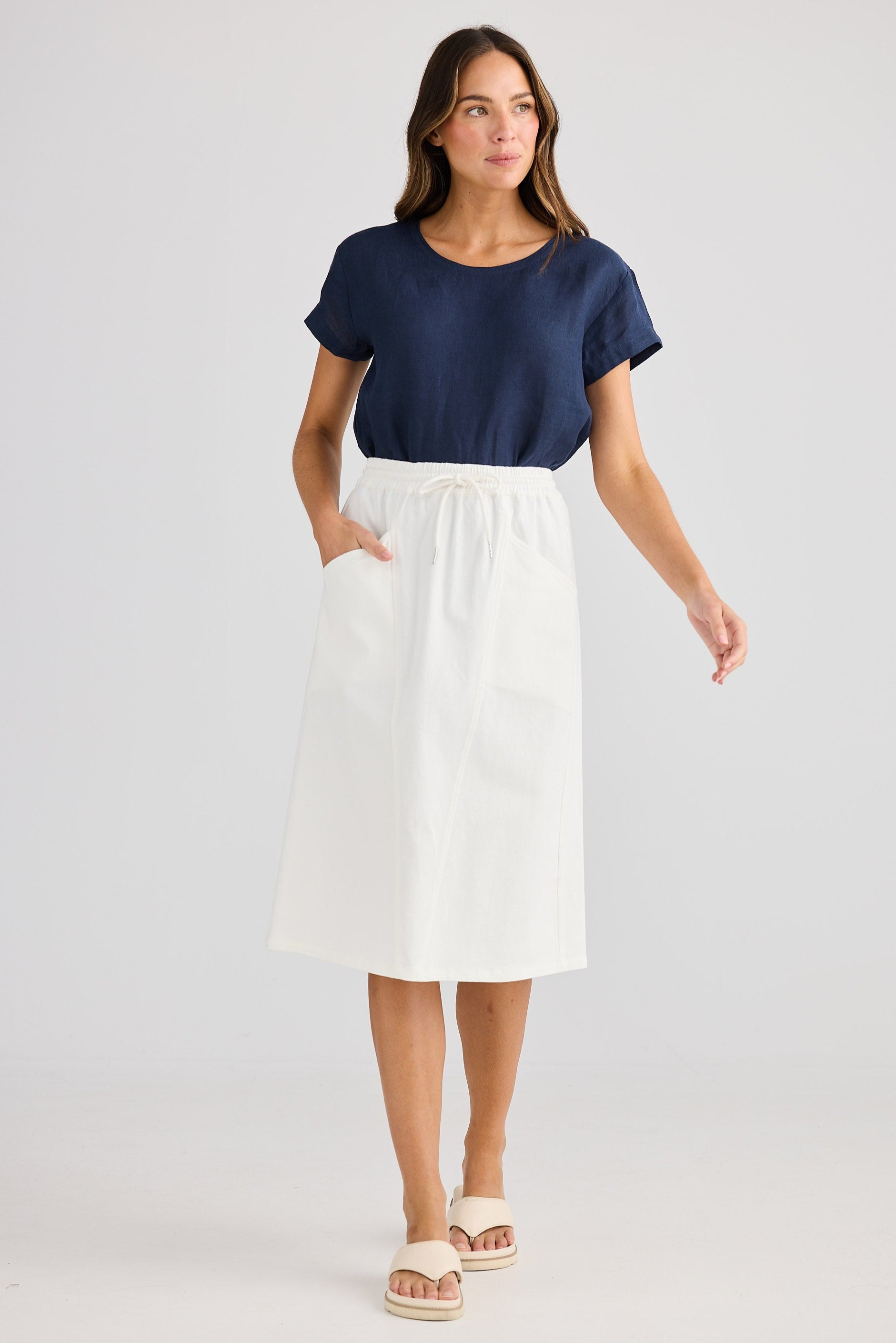 Woman wearing a navy top and white skirt on a plain background