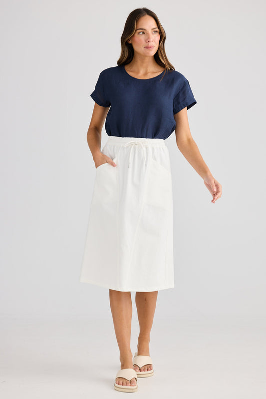 Woman wearing a navy top and white skirt on a plain background