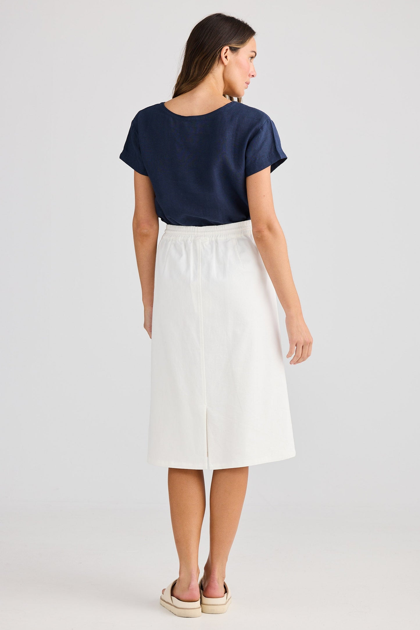 Woman wearing a navy top and white skirt on a plain background