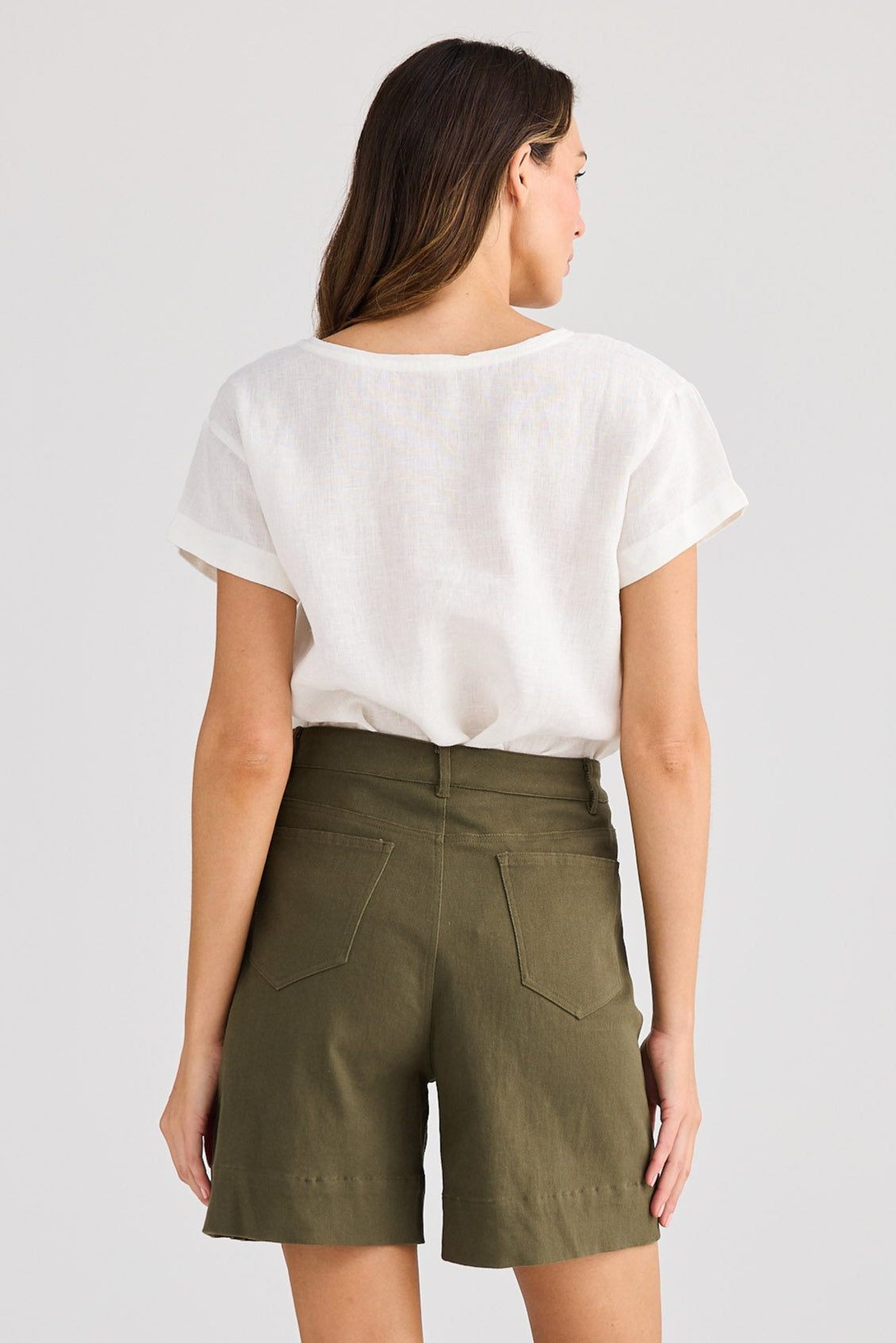 Woman wearing olive green shorts and a white top on a light gray background