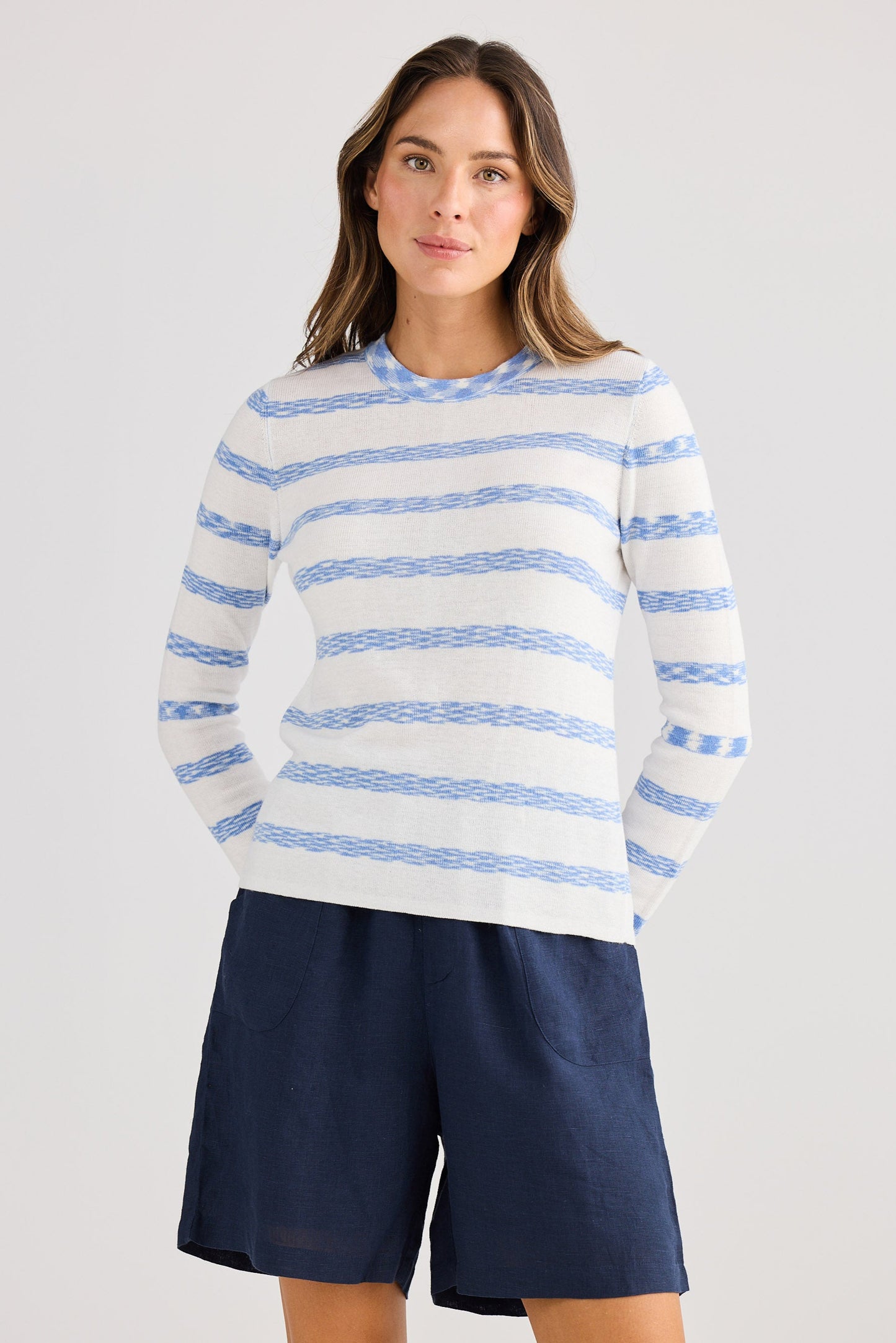Woman wearing a striped sweater and navy shorts on a light gray background