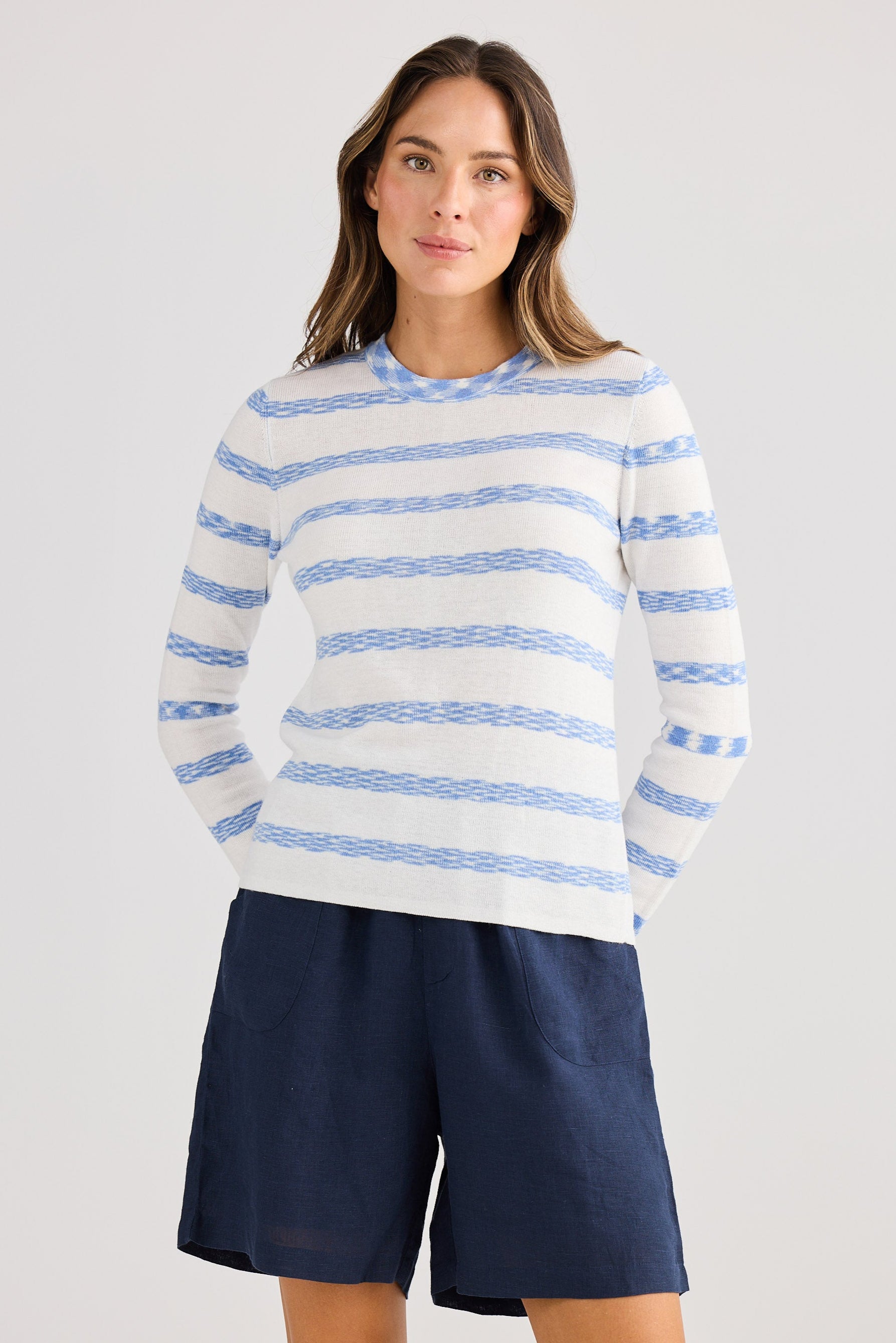 Woman wearing a striped sweater and navy shorts on a light gray background