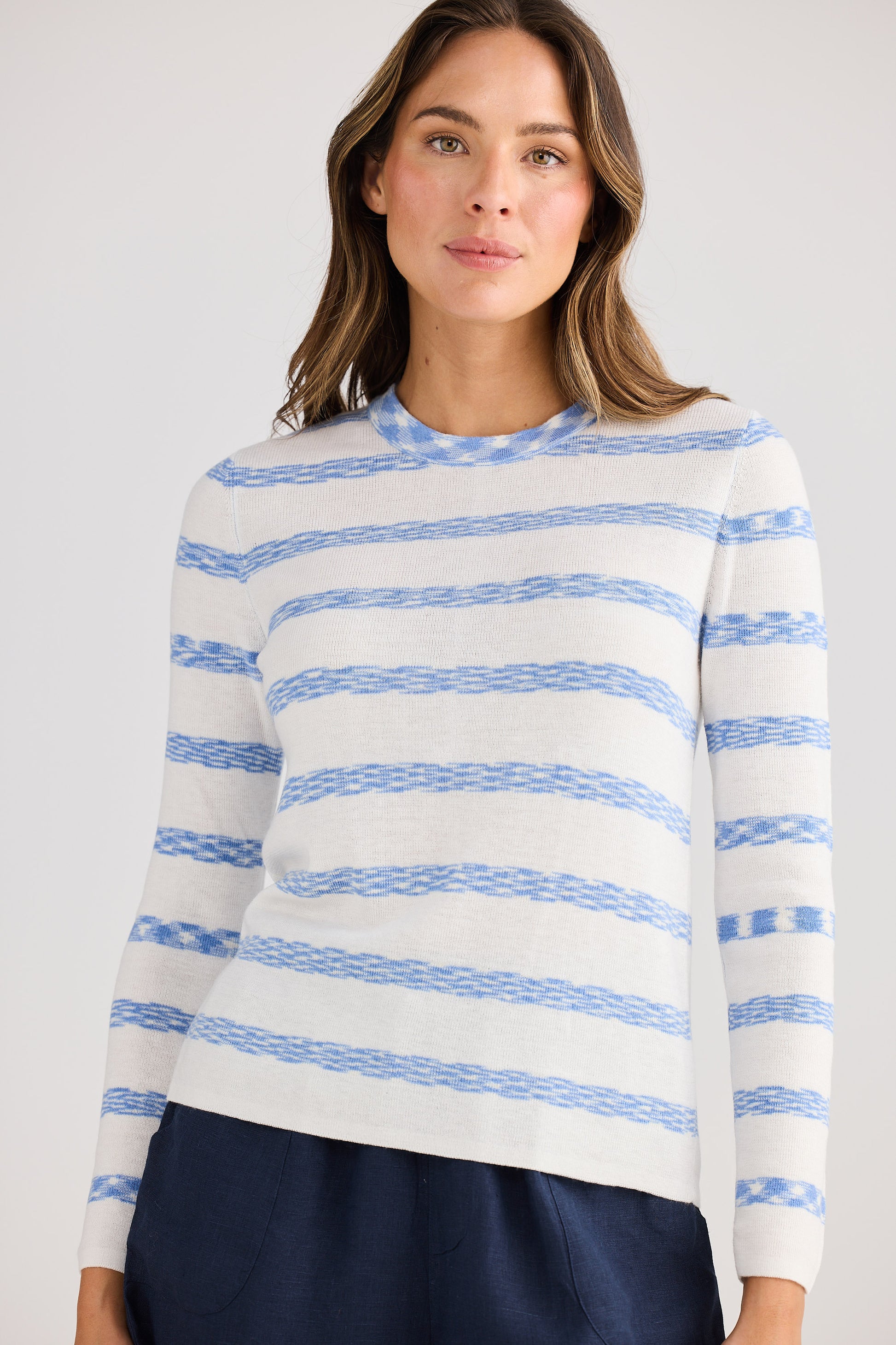 Woman wearing a white sweater with blue stripes against a plain background