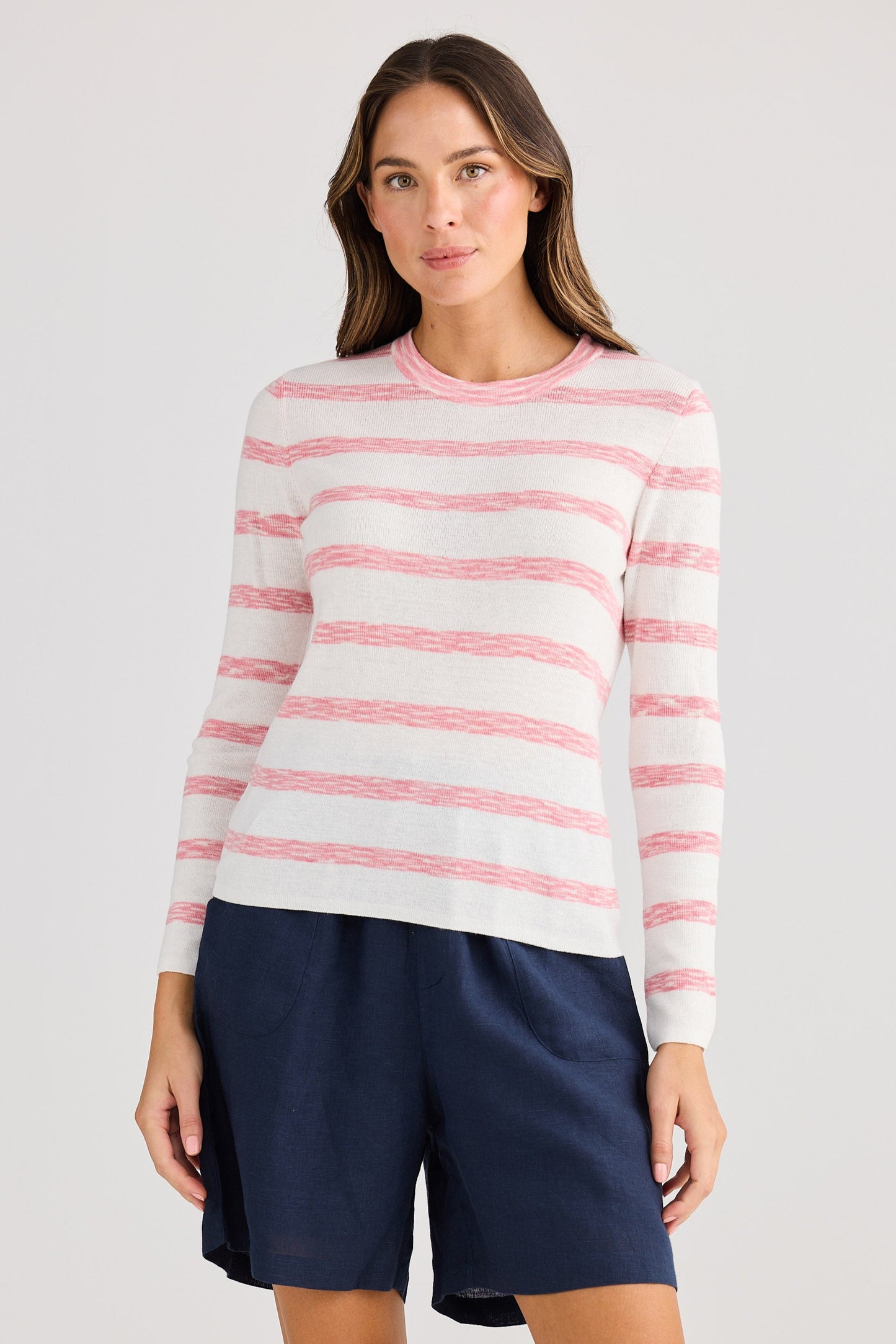 Woman wearing a striped sweater and navy shorts on a plain background