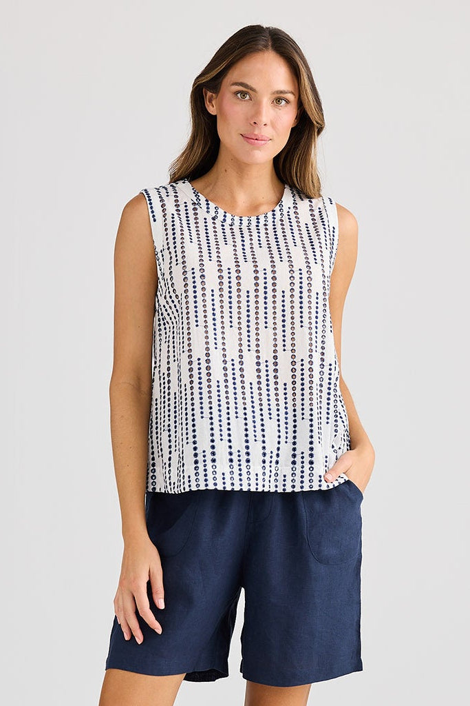 Woman wearing a sleeveless patterned top and navy shorts on a white background