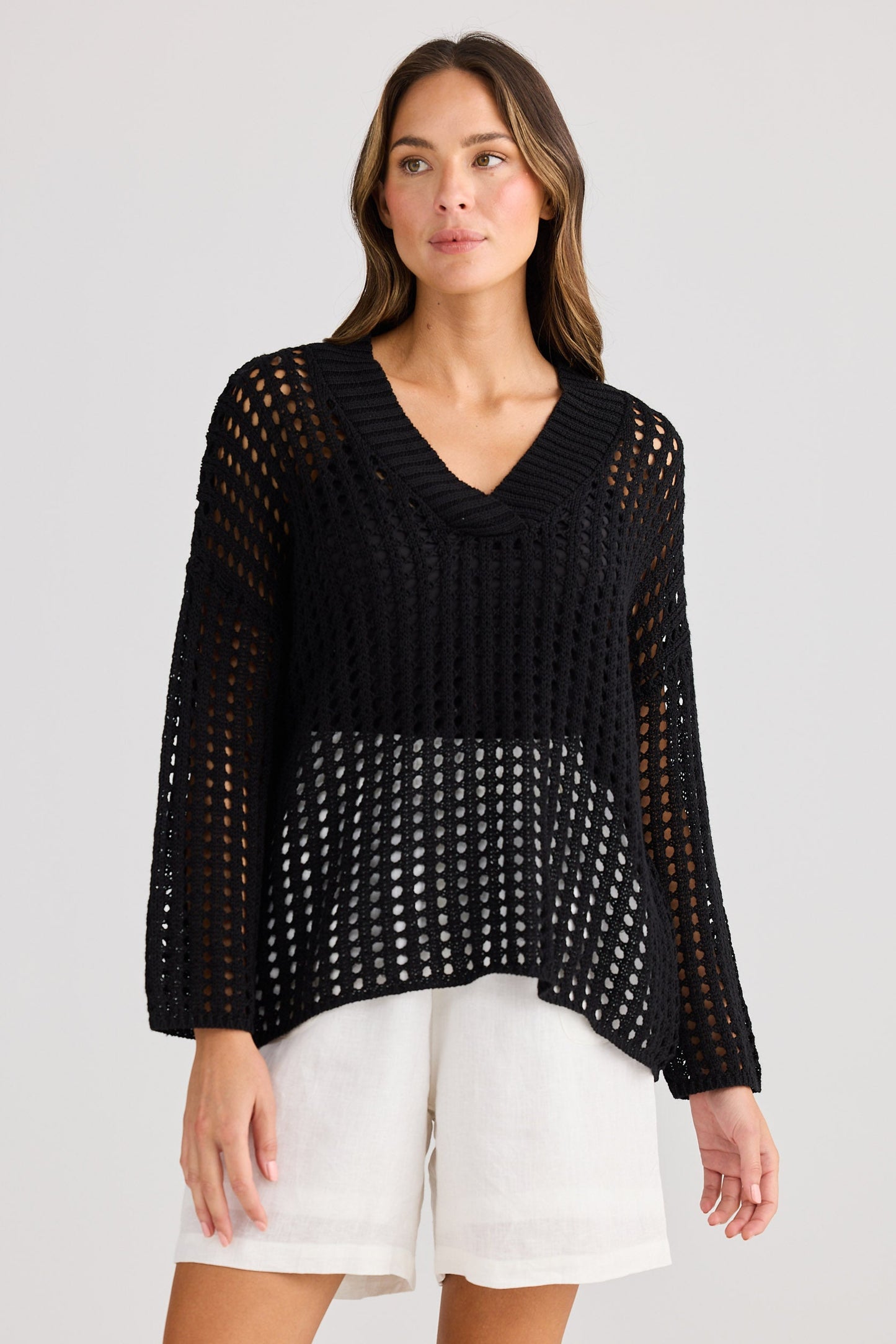 Woman wearing a black knit top and white shorts on a plain background