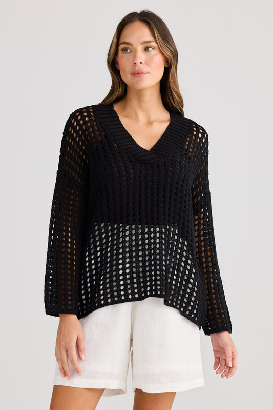 Woman wearing a black knit top and white shorts on a plain background