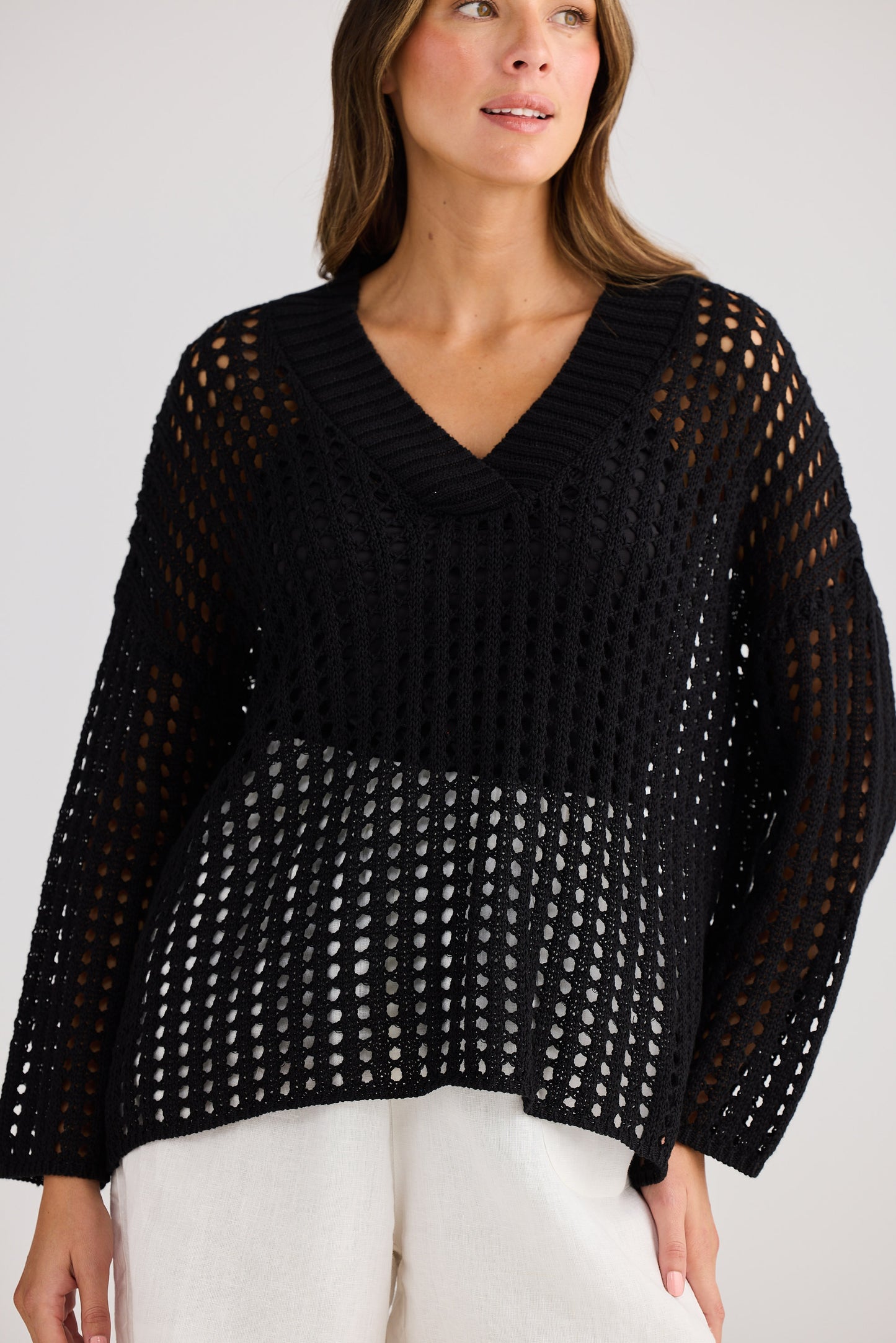 Woman wearing a black open-knit sweater against a plain background