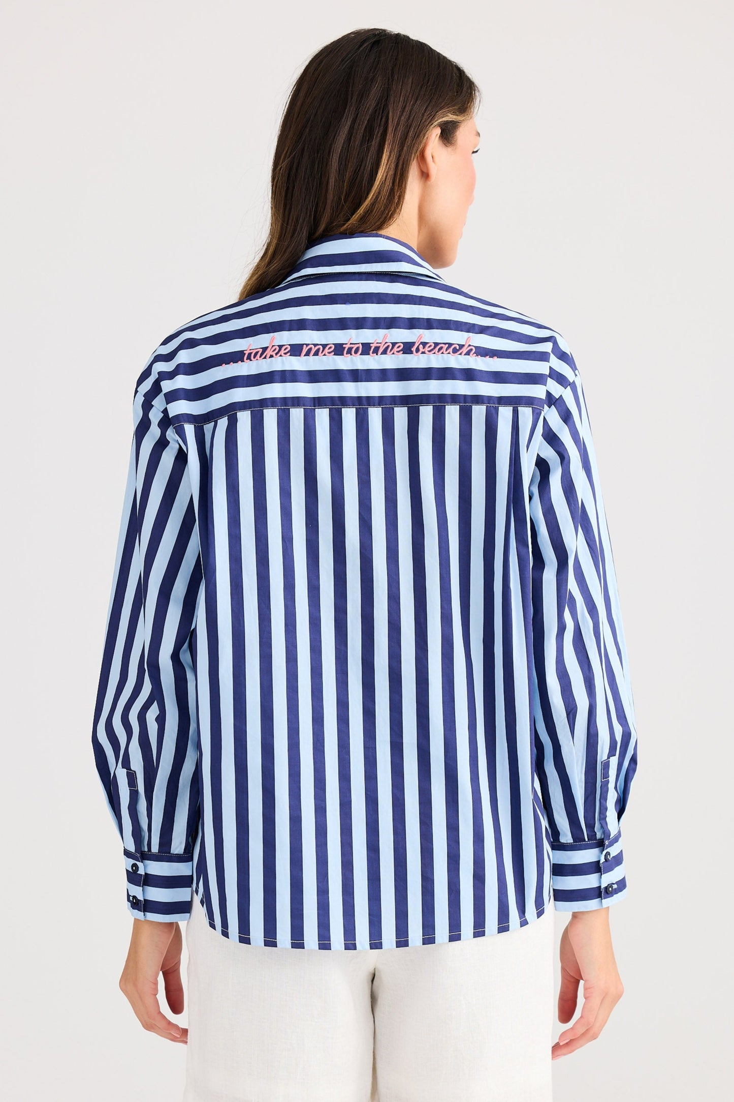 Woman wearing a blue and white striped shirt and white shorts on a light gray background