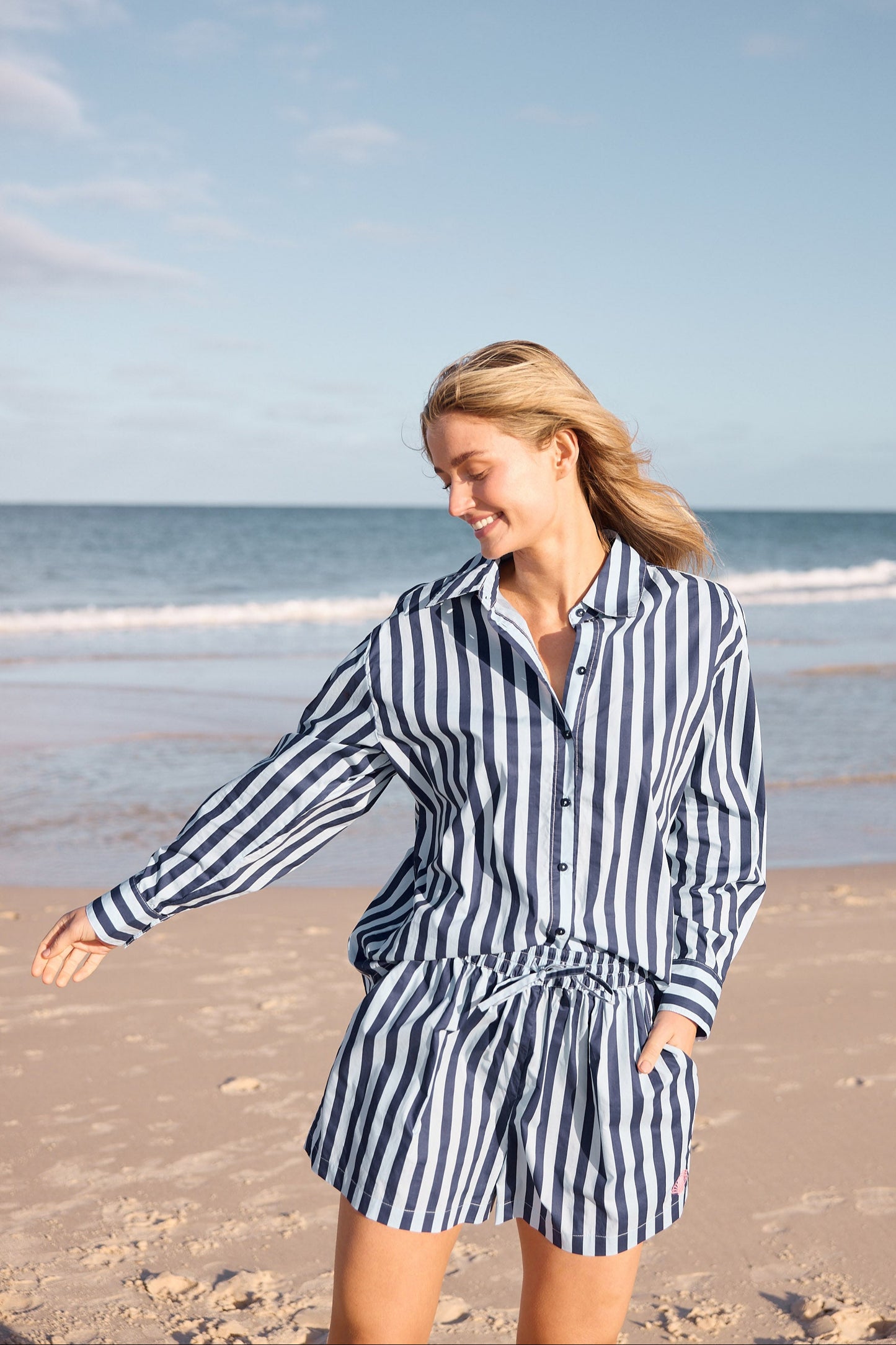 Woman in a striped outfit standing on a beach with ocean and sky in the background