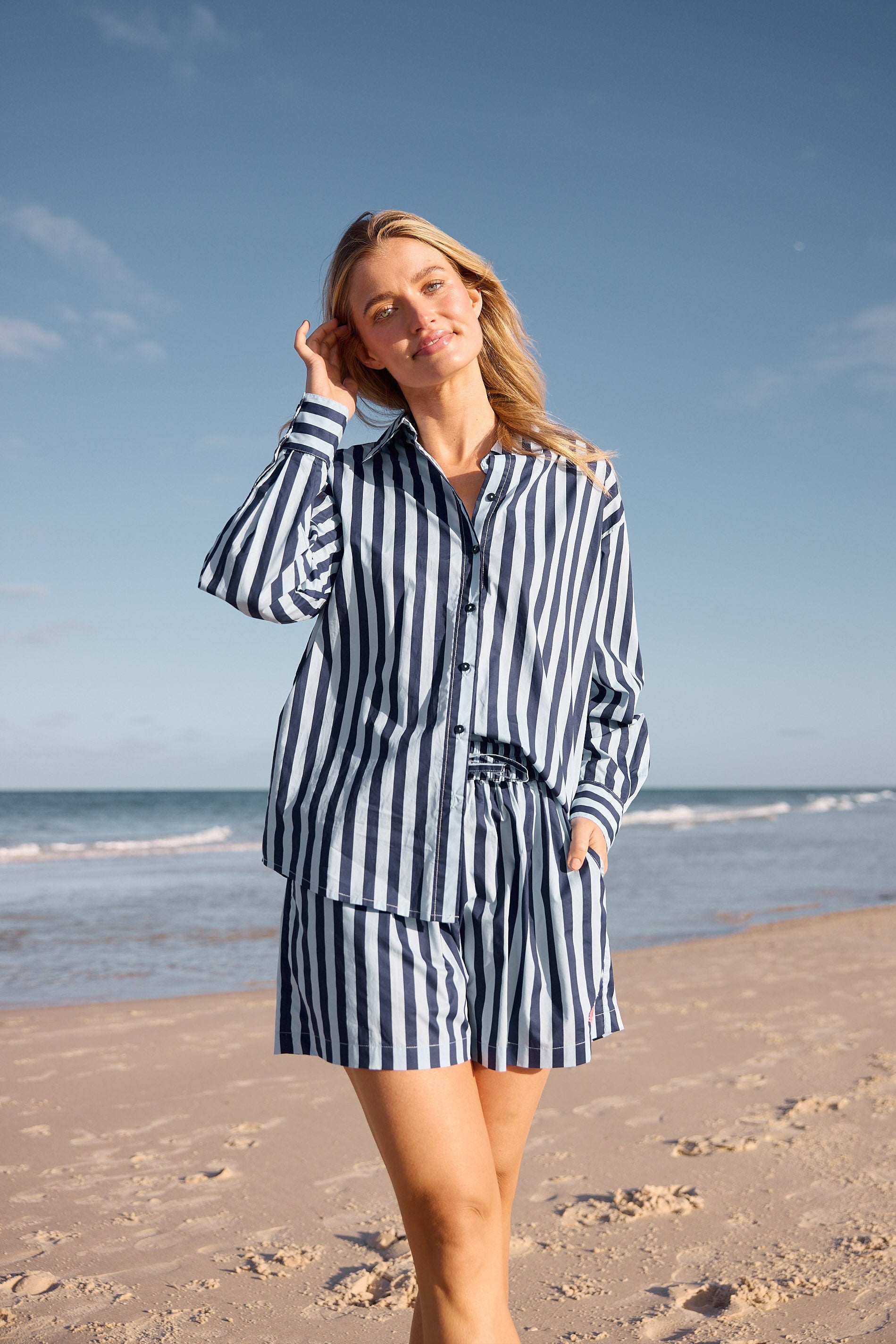 Woman in a striped outfit standing on a beach with ocean and sky in the background