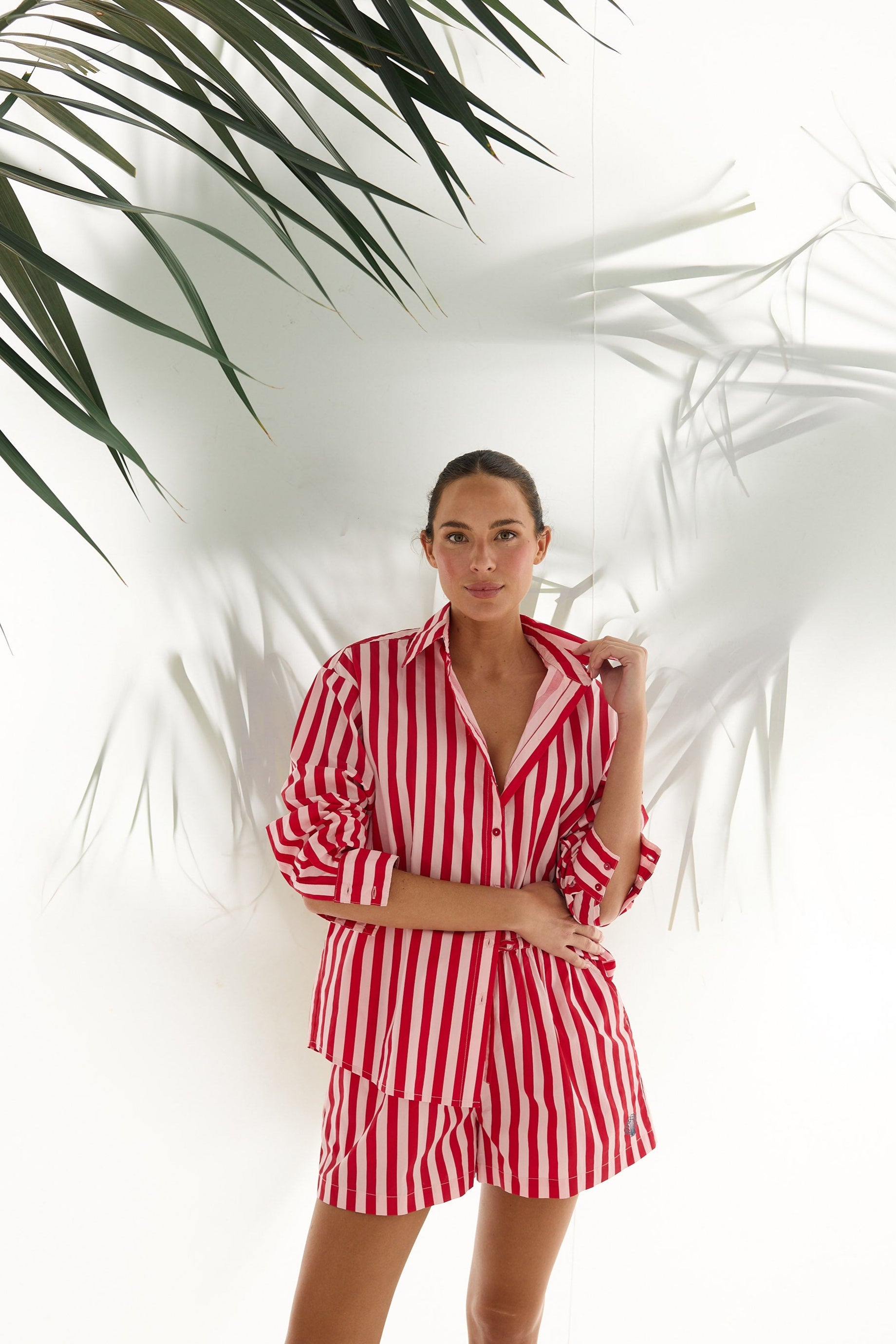 Woman wearing a red and white striped outfit standing against a white background with green leaves.