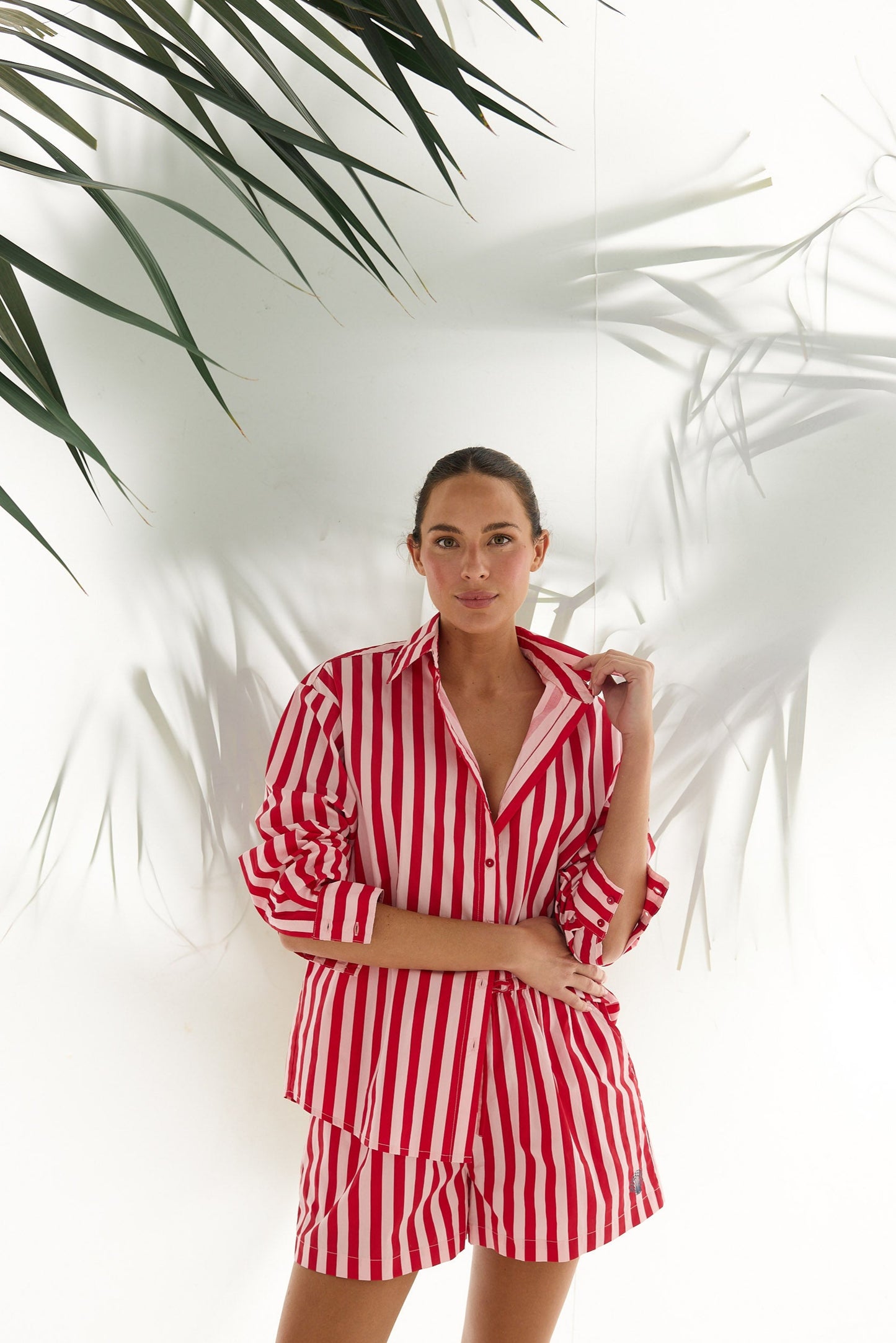 Woman wearing a red and white striped outfit standing against a white background with green leaves.