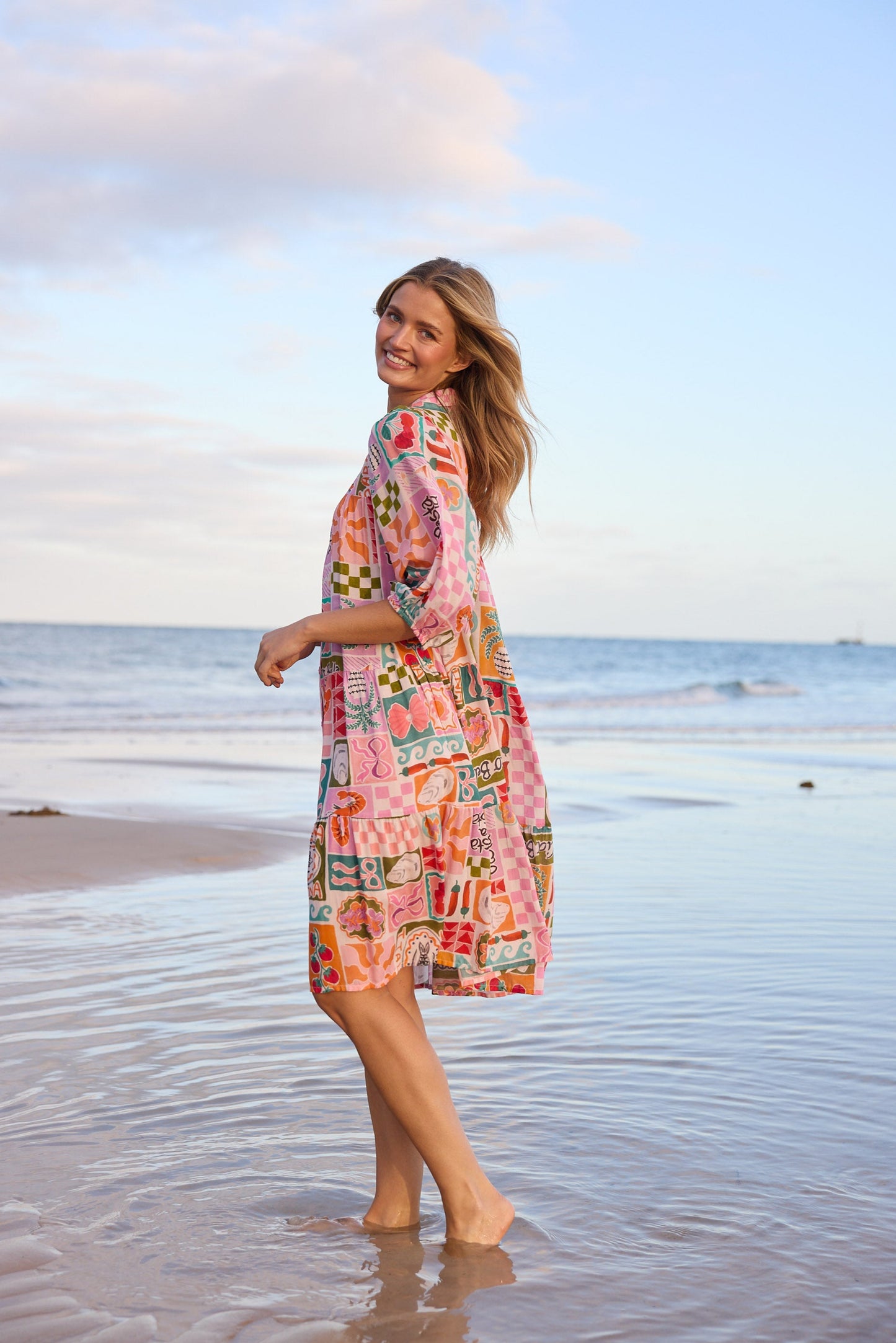Woman in a colorful dress standing on a beach with ocean and sky in the background