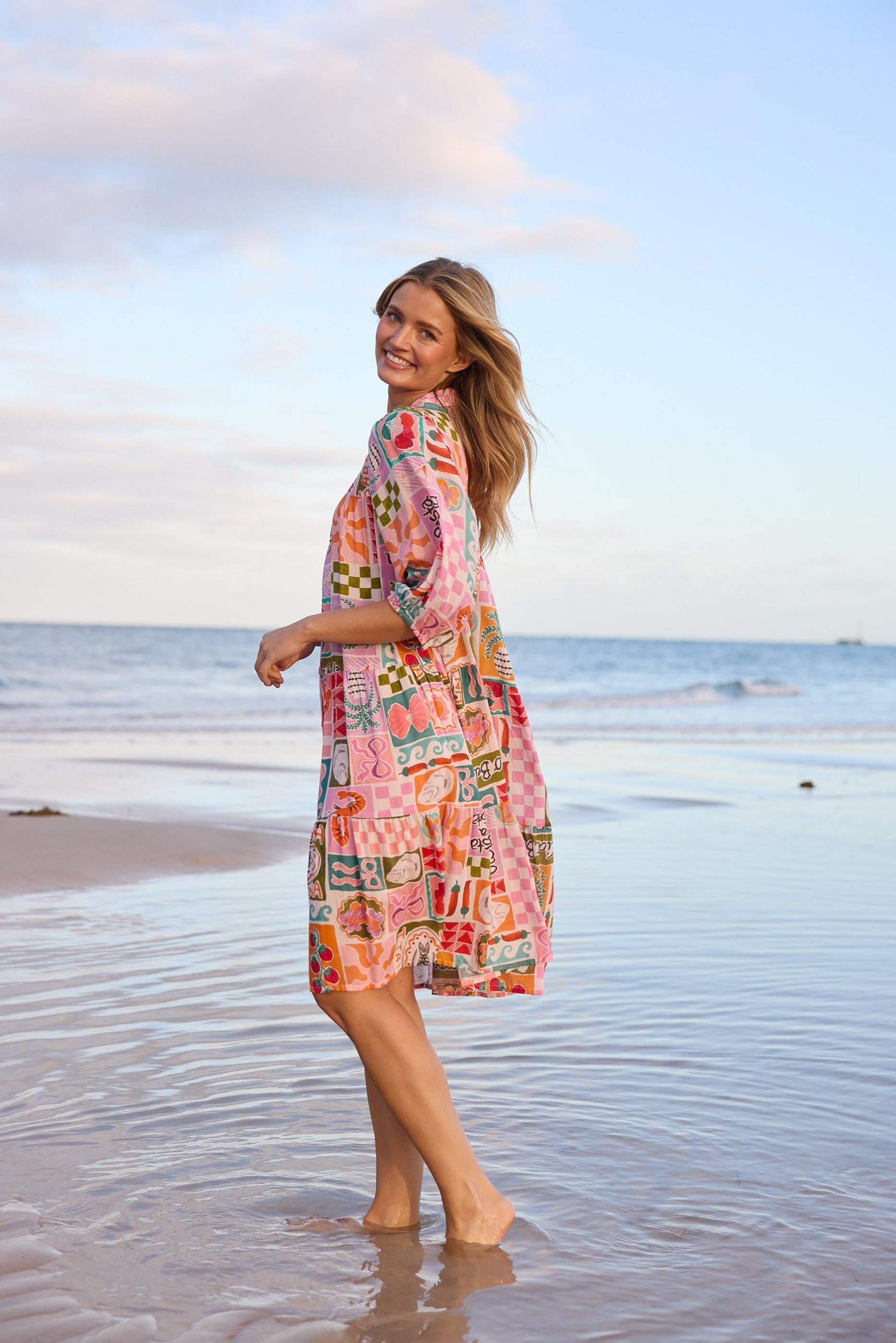 Woman in a colorful dress standing on a beach with ocean and sky in the background