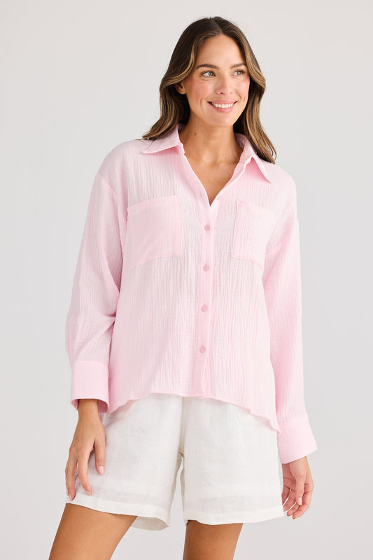Woman wearing a pink button-up shirt and white shorts on a plain background