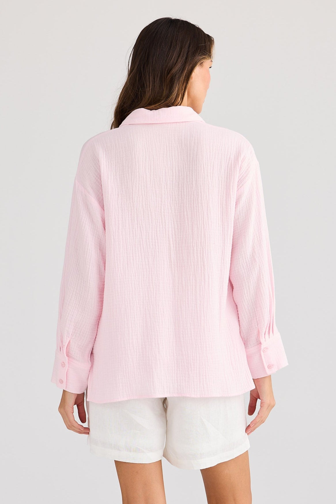 Person wearing a light pink long-sleeve shirt and white shorts on a plain background