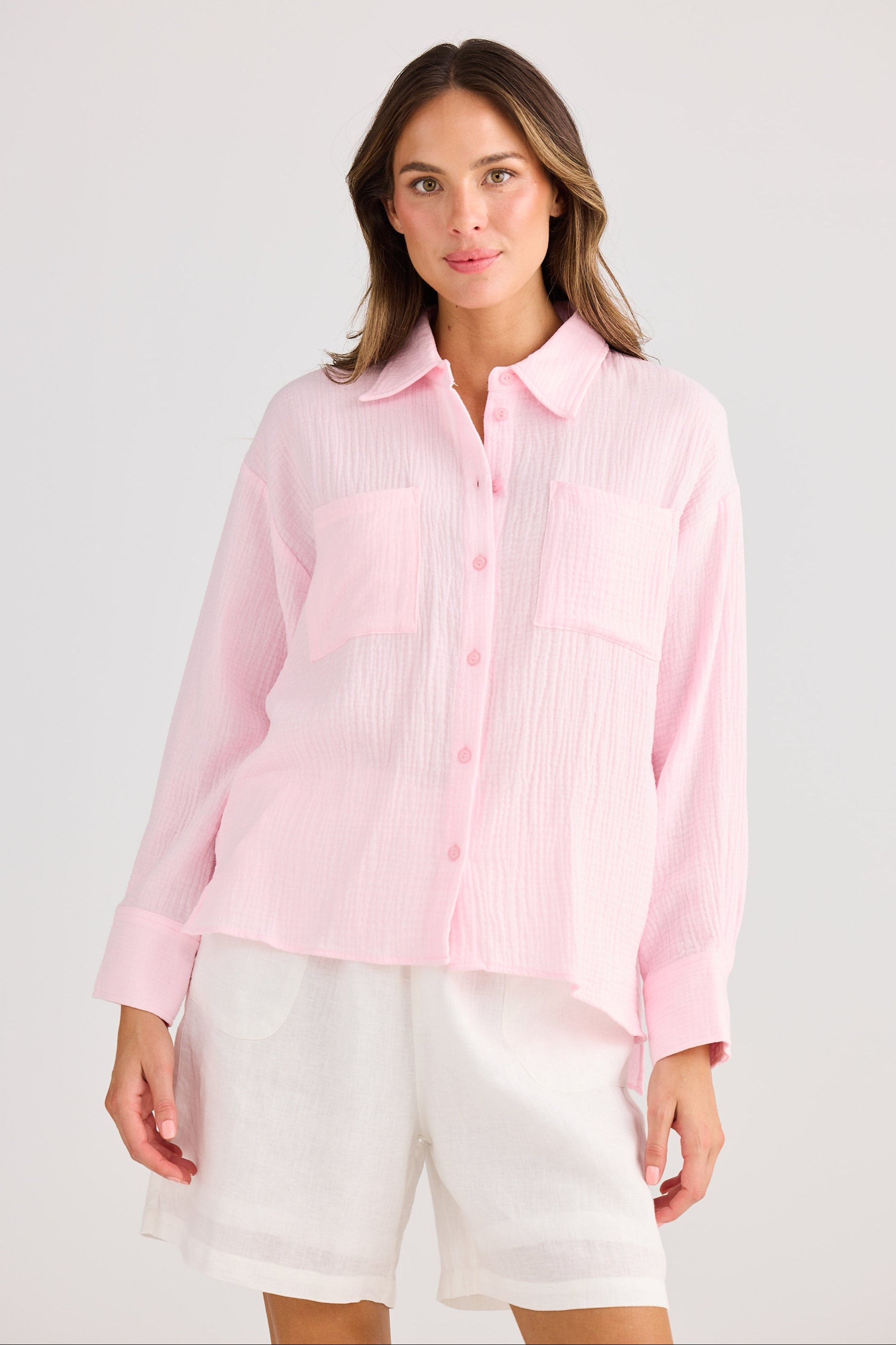 Woman wearing a light pink button-up shirt and white shorts on a plain background