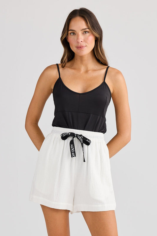 Woman wearing a black tank top and white shorts on a plain background