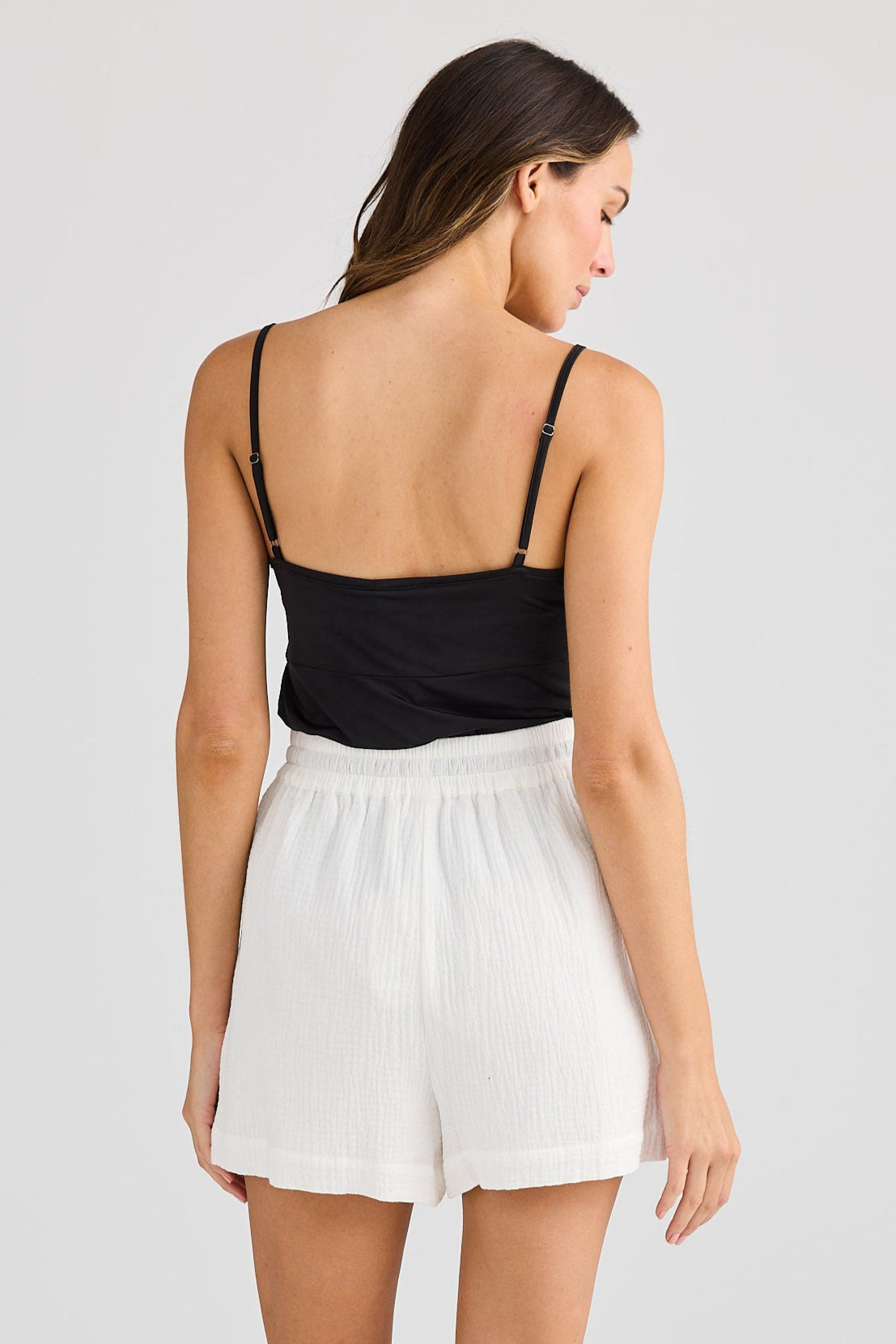 Woman wearing a black top and white shorts on a plain background