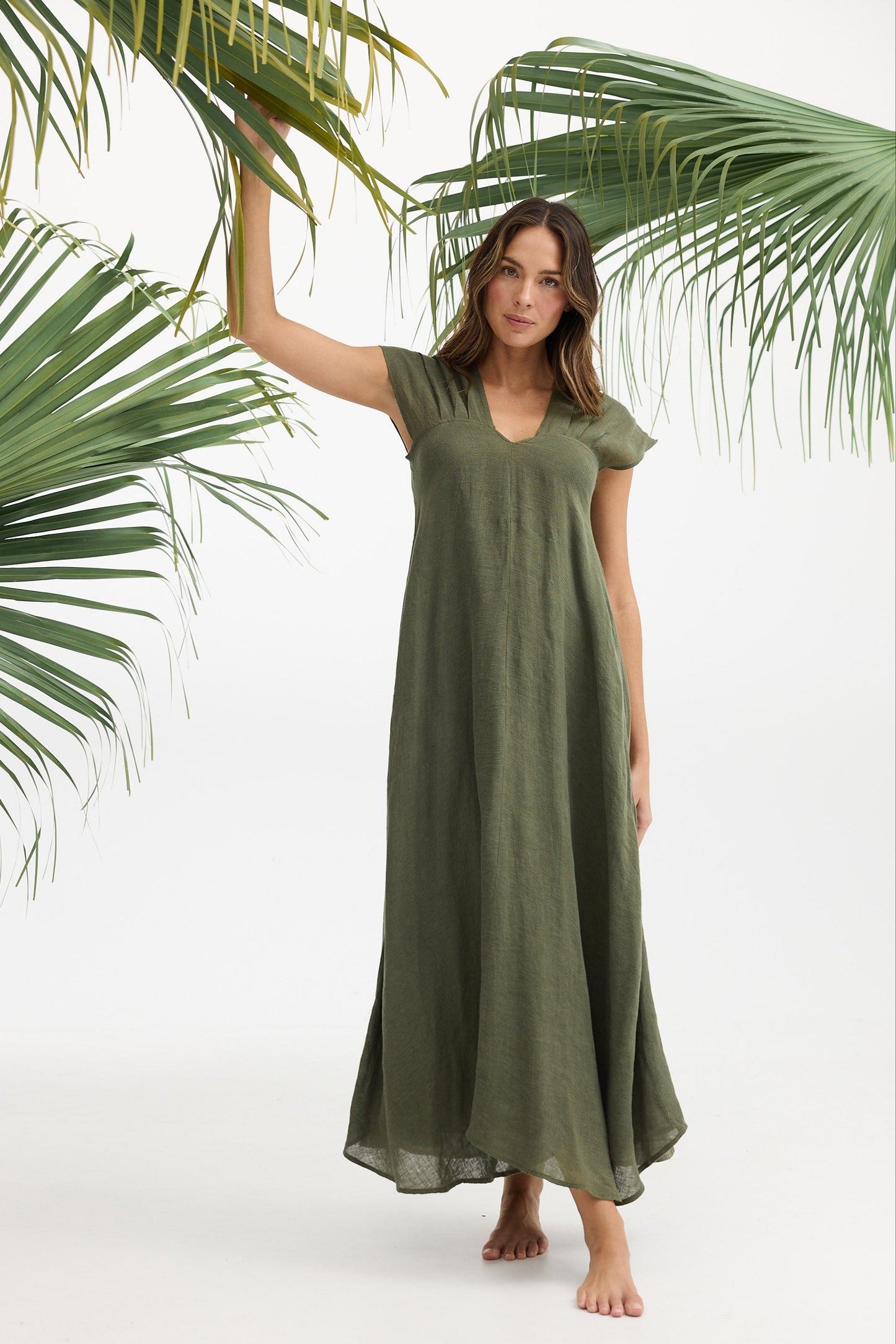 Woman wearing a green dress standing under palm leaves on a white background