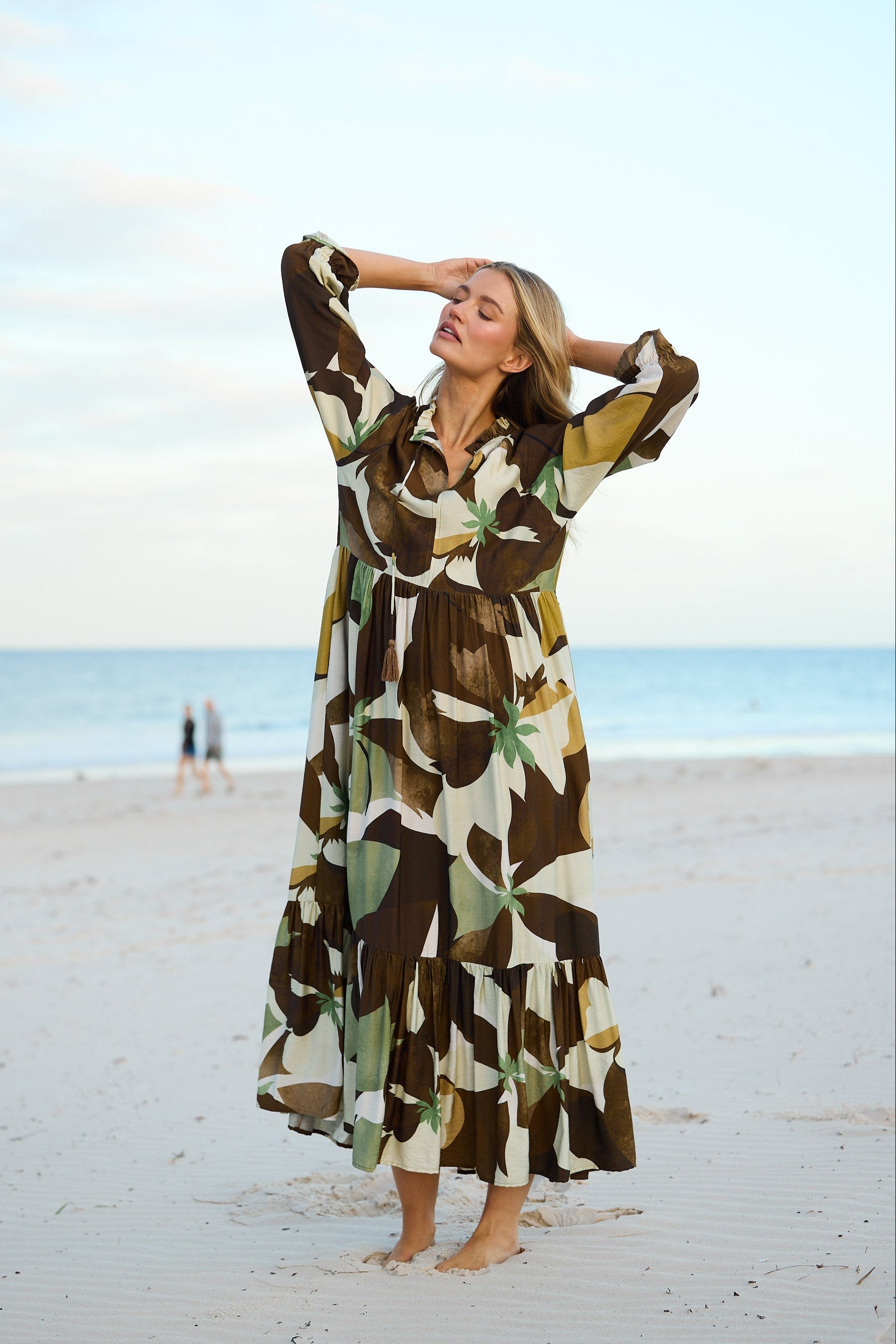 Woman in a patterned dress standing on a beach with a clear sky.