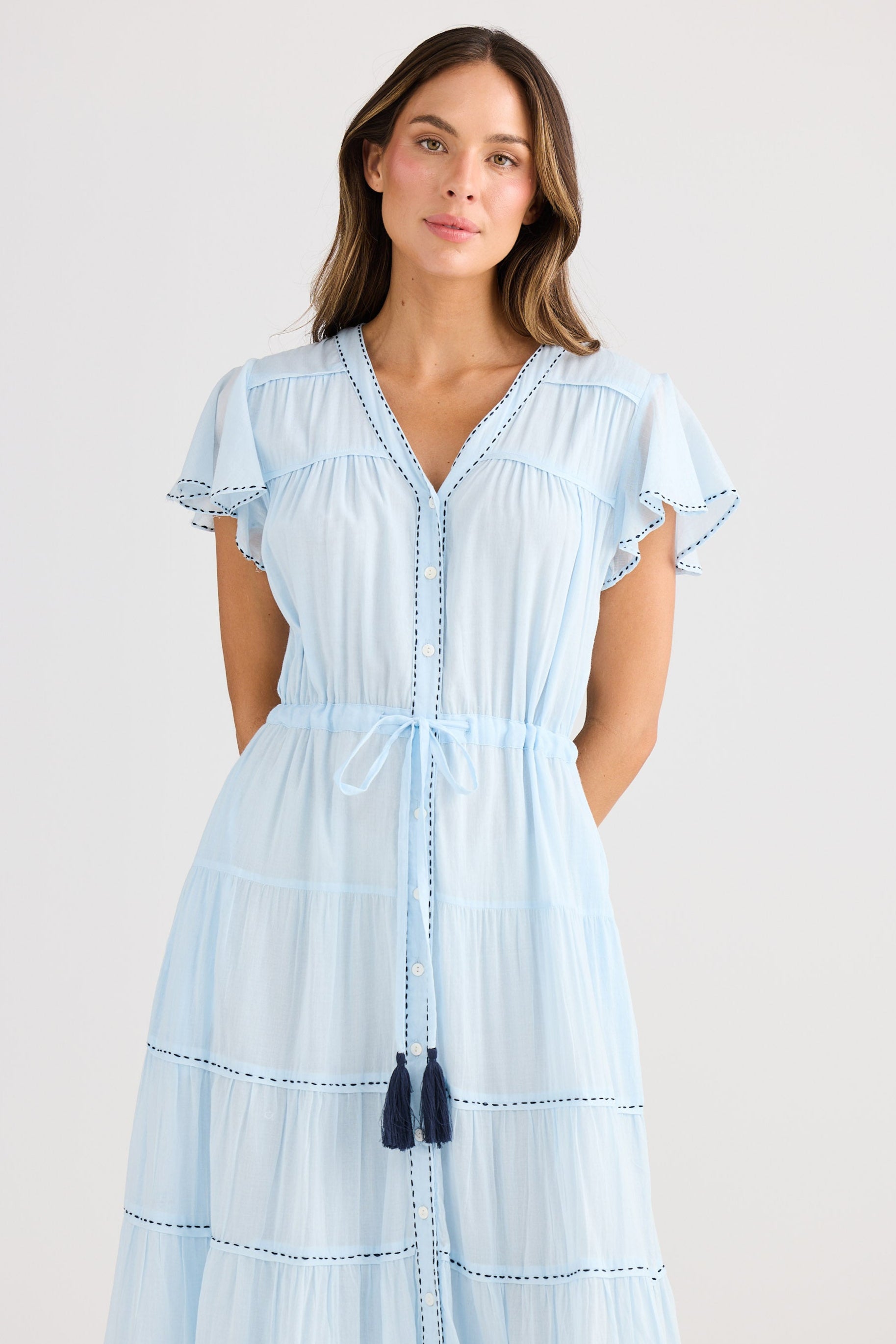 Woman wearing a light blue dress with tassel details on a plain background