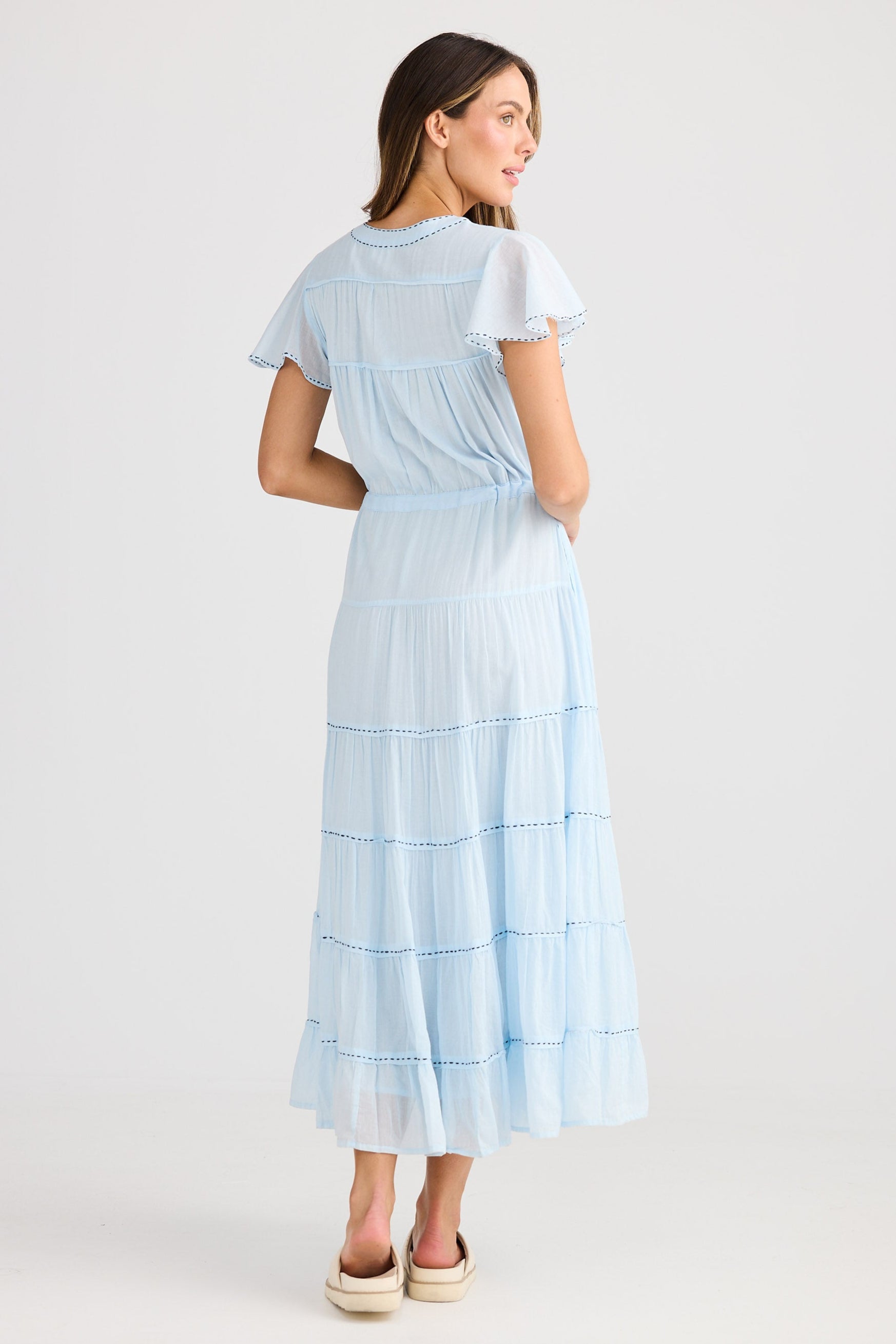 Woman wearing a light blue dress with white stripes on a plain background