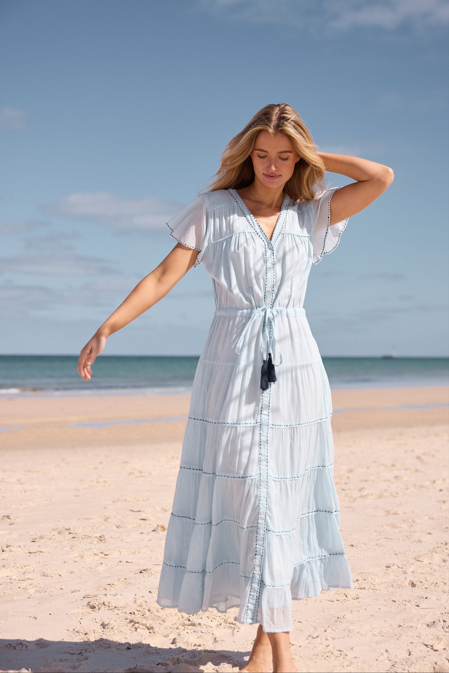 Woman in a light blue dress standing on a beach with ocean and sky in the background