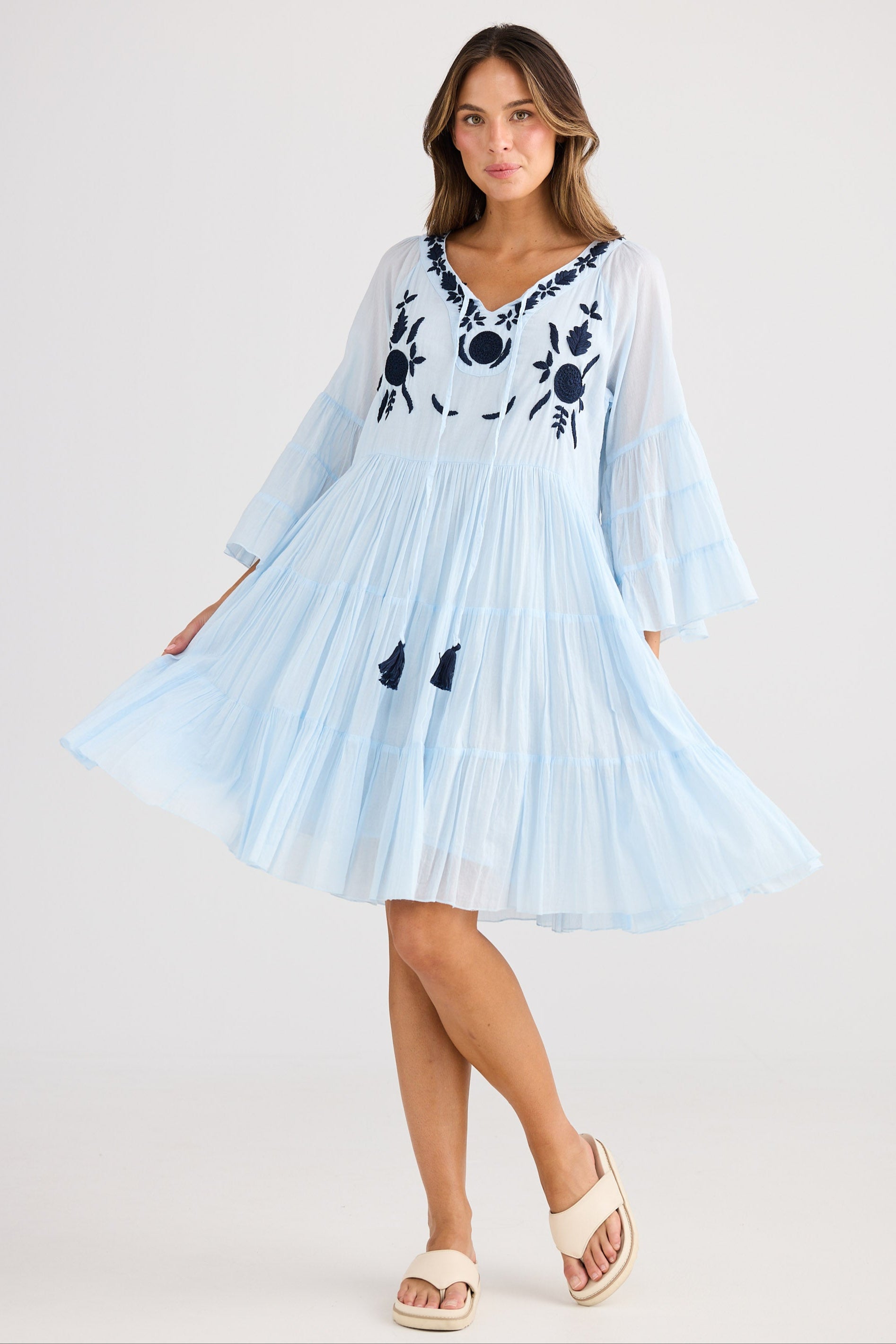 Woman wearing a light blue dress with black floral embroidery on a white background