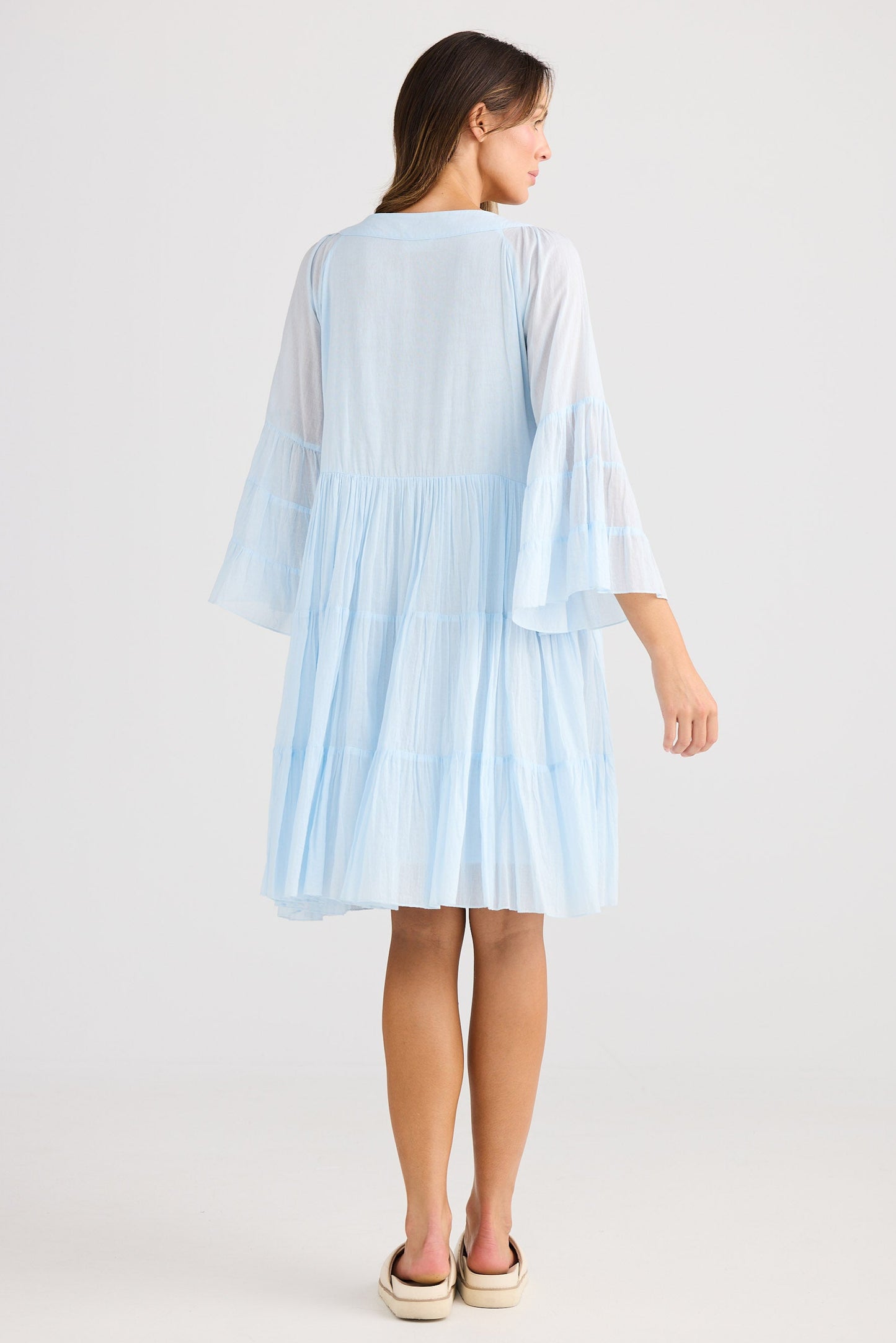 Woman wearing a light blue dress with sheer sleeves on a white background