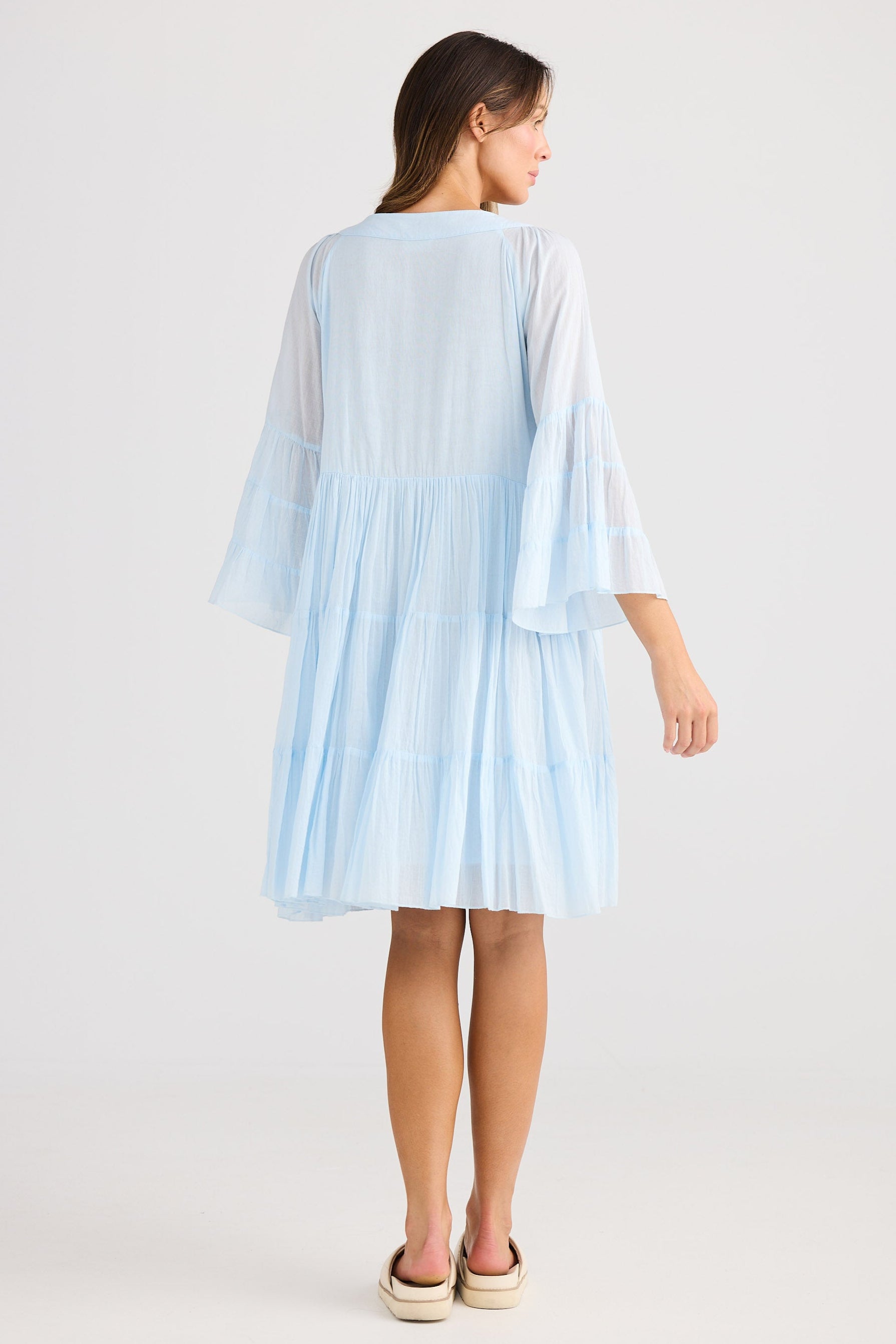 Woman wearing a light blue dress with sheer sleeves on a white background