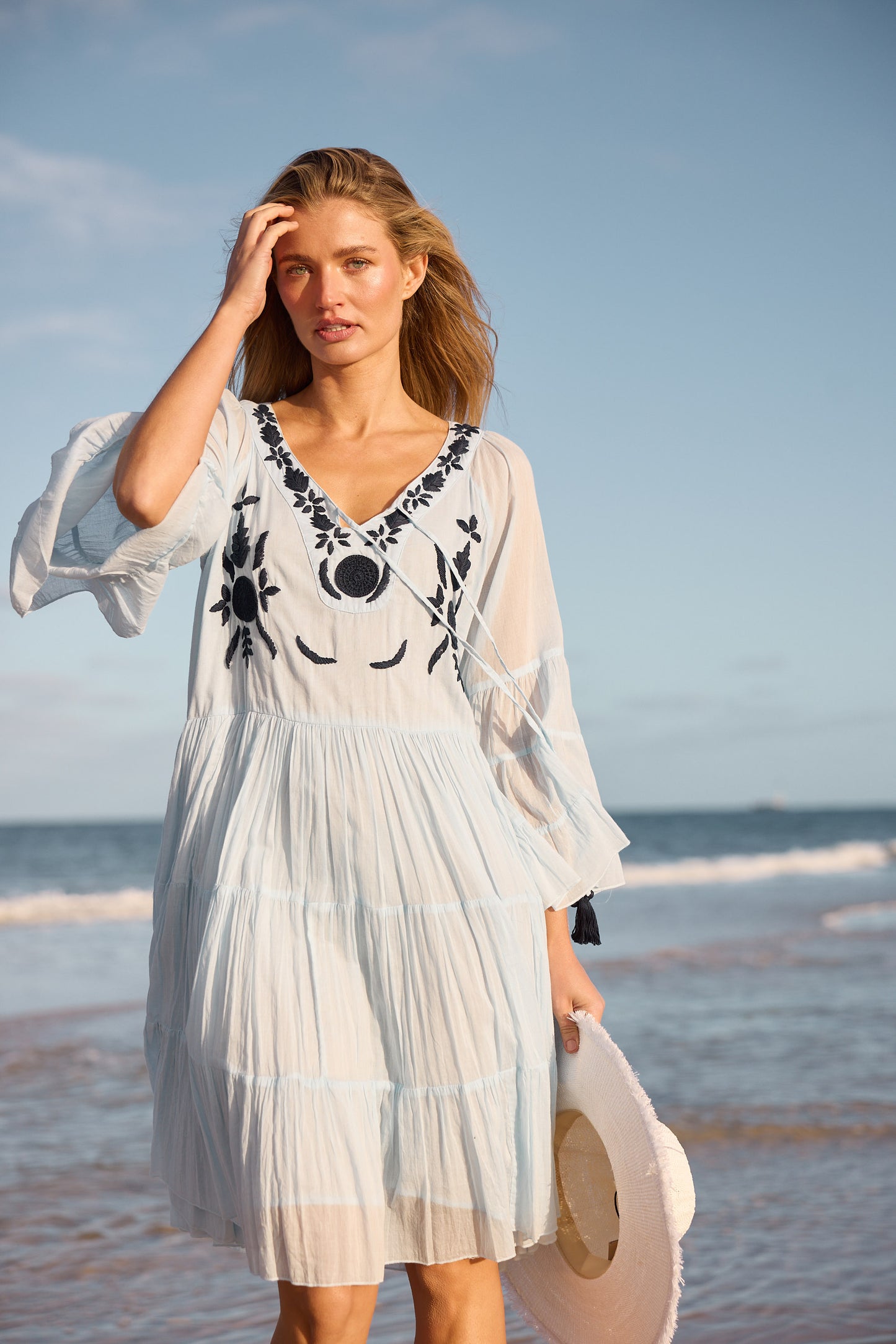 Woman in a light blue dress with black embroidery on a beach