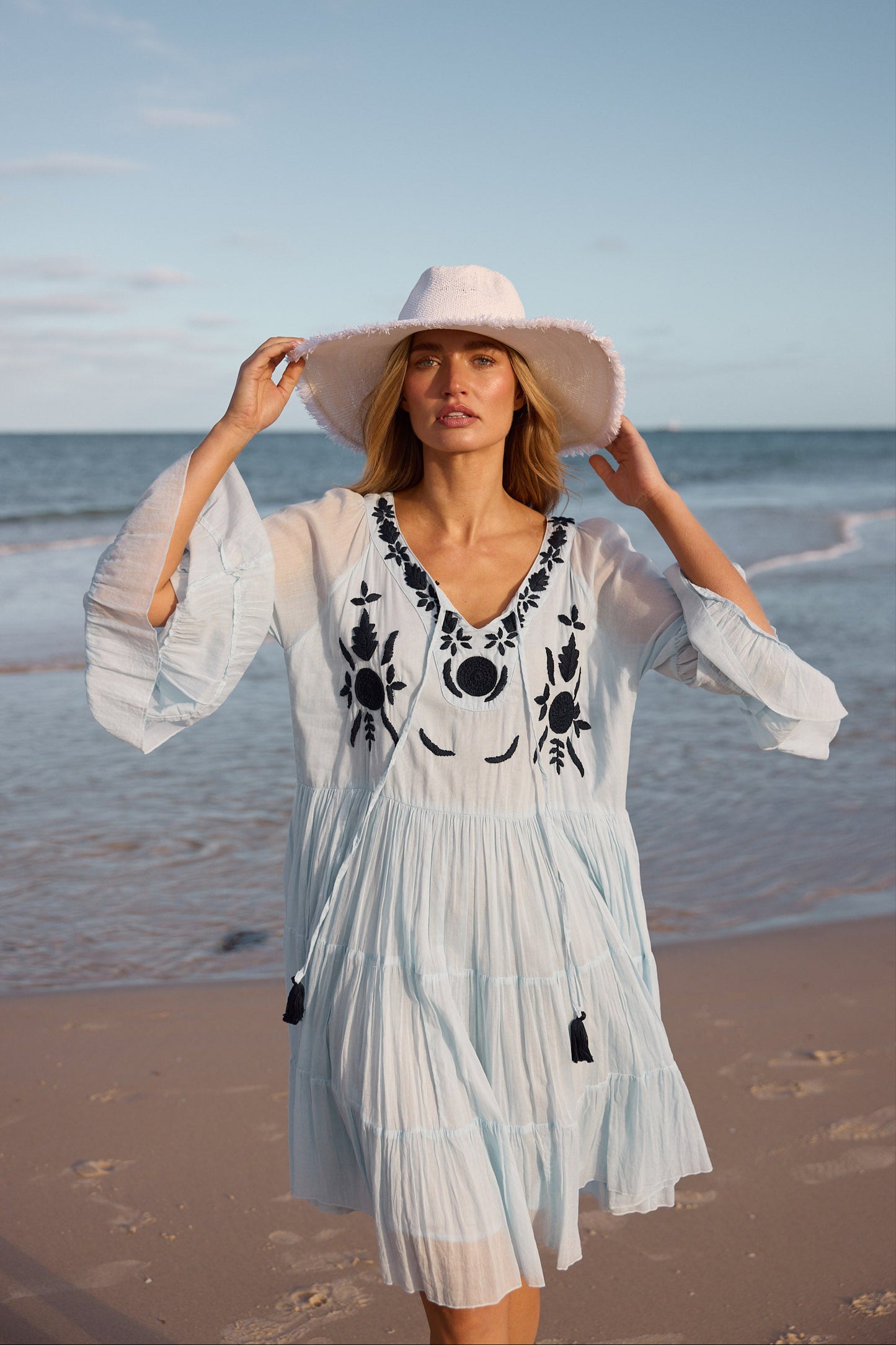 Woman in a light blue dress with black embroidery on a beach