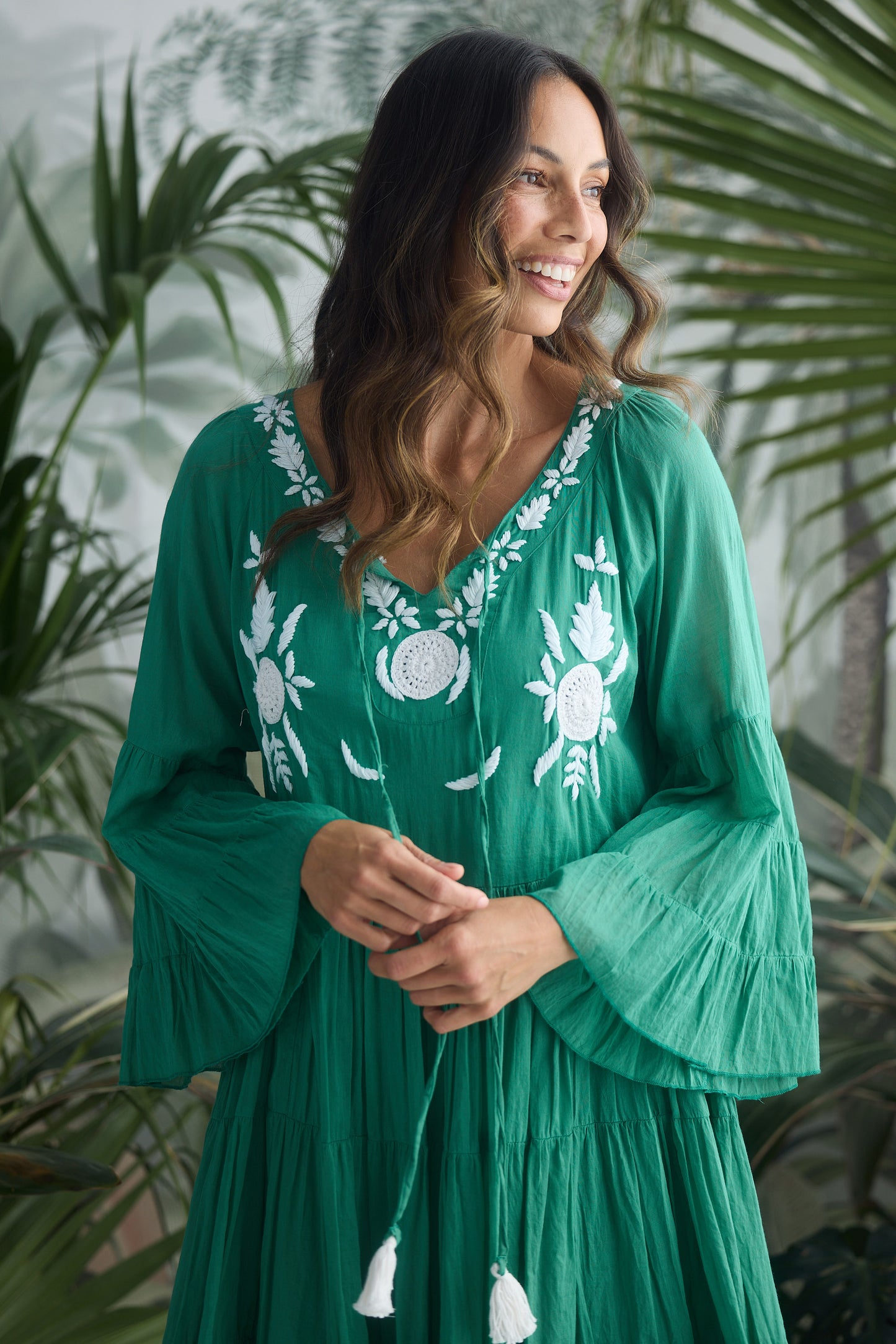 Woman wearing a green dress with white embroidery against a leafy background