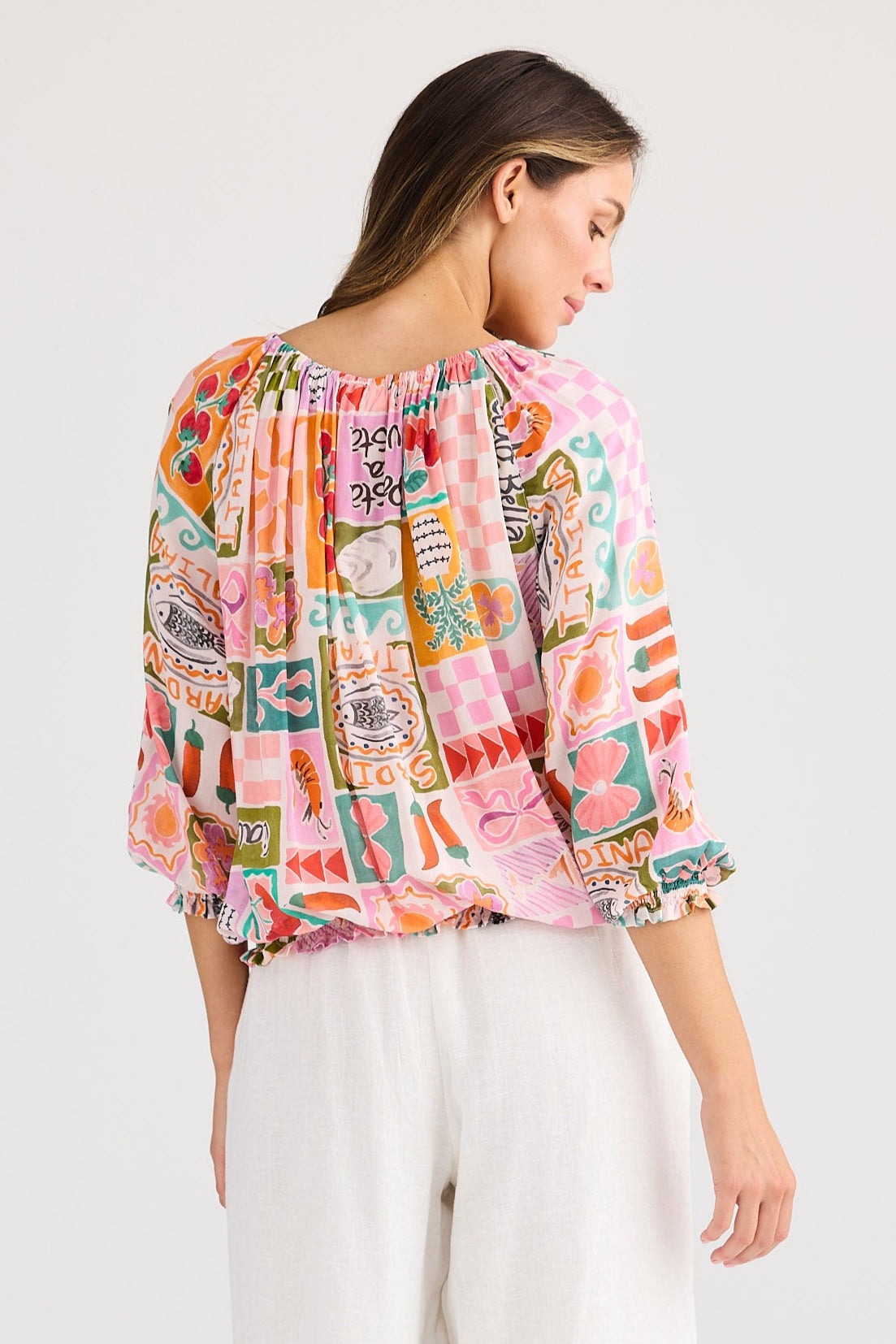 Woman wearing a colorful patterned blouse and white pants on a white background
