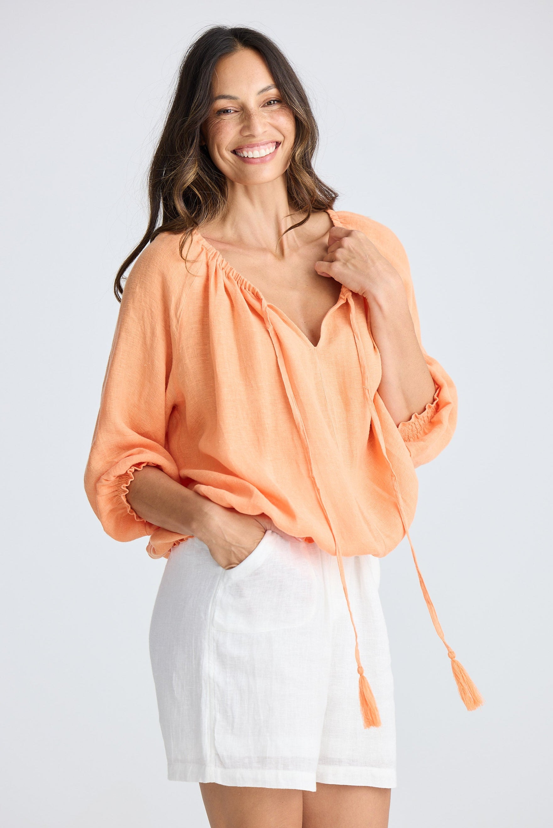 Woman wearing an orange top and white shorts on a plain background