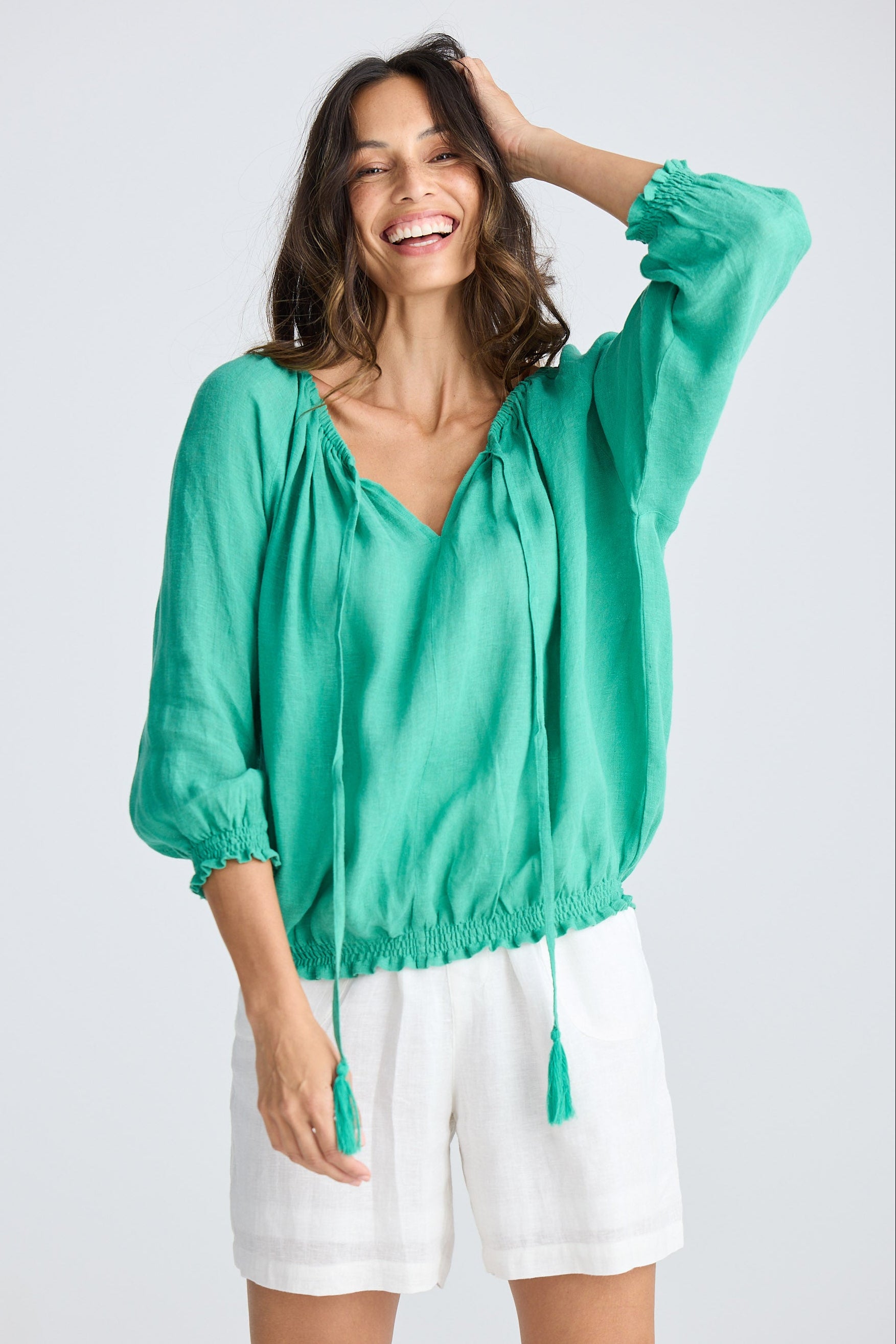 Woman wearing a green blouse and white shorts on a light gray background