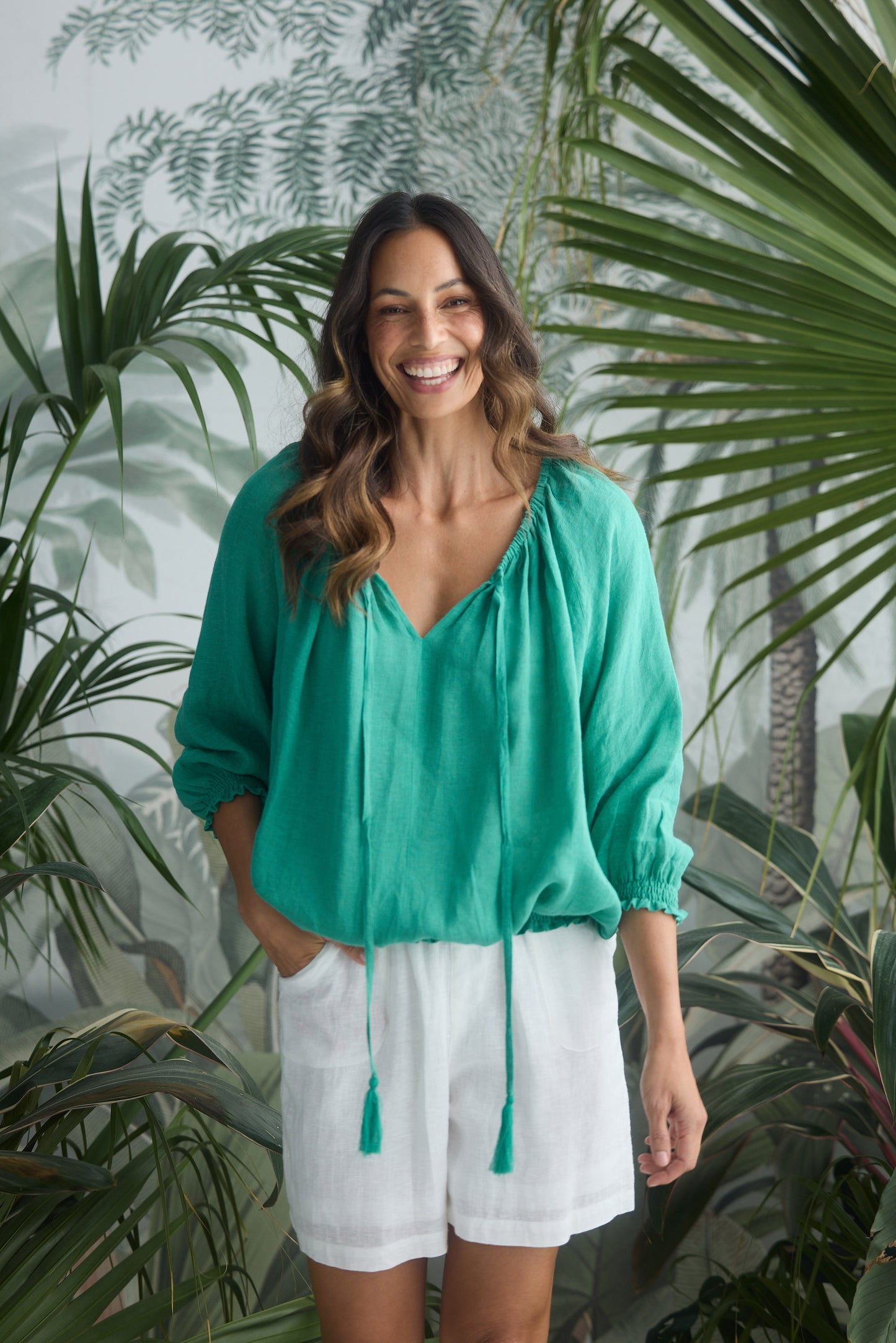 Woman wearing a green blouse and white shorts standing in front of a leafy background