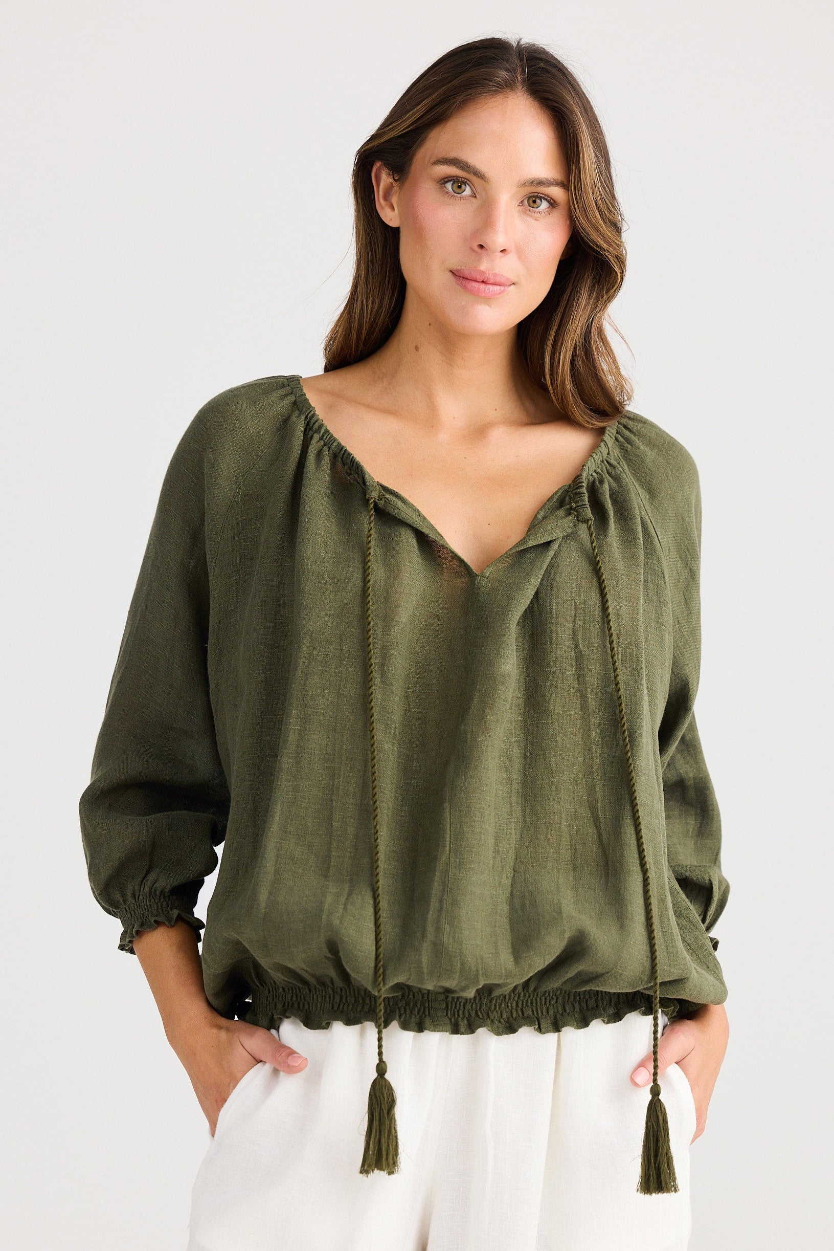 Woman wearing an olive green blouse with tassels on a white background