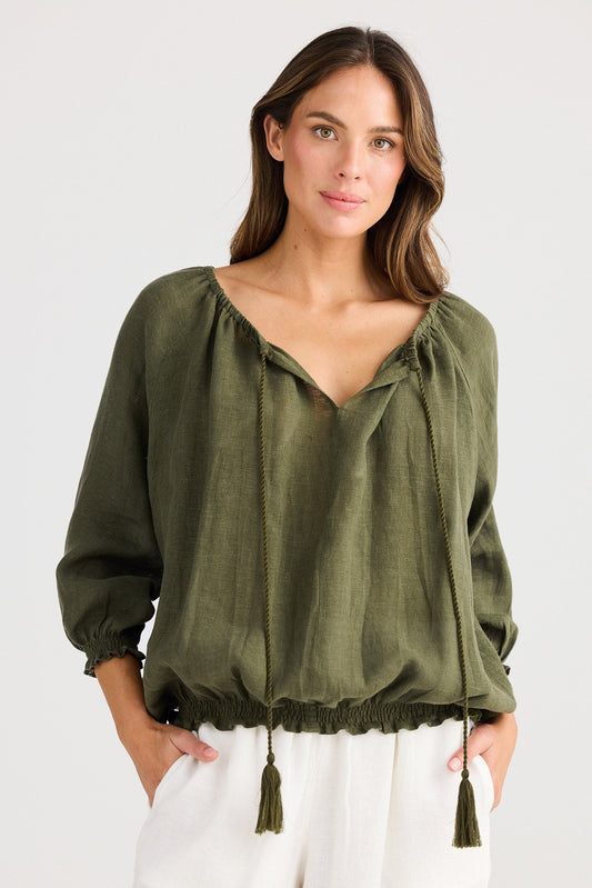 Woman wearing an olive green blouse with tassels on a white background