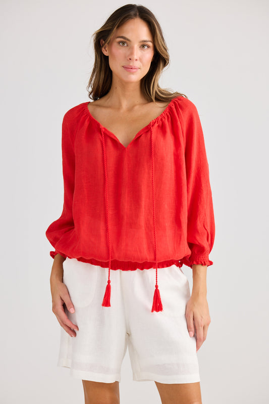 Woman wearing a red blouse with tassels and white shorts on a white background
