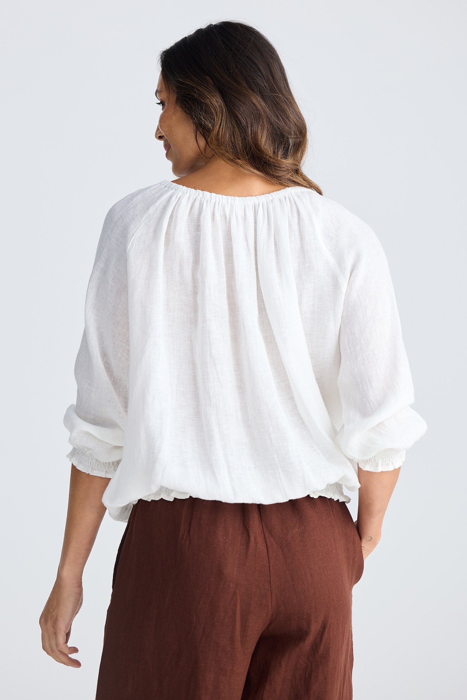 Woman wearing a white blouse and brown pants on a white background