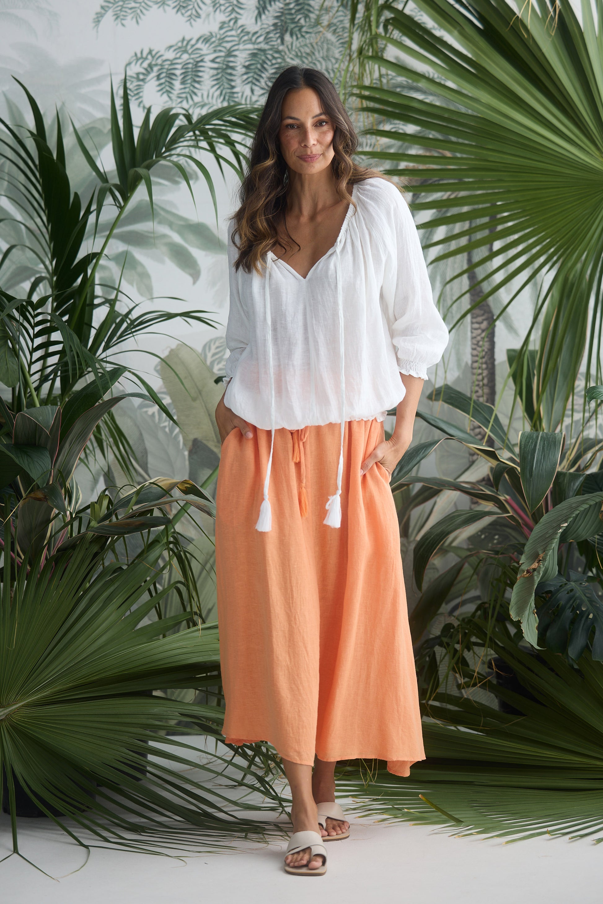 Woman in a white blouse and peach skirt standing among tropical plants