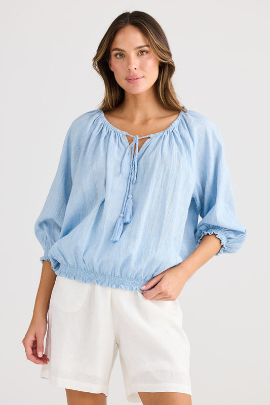 Woman wearing a light blue blouse with balloon sleeves and white shorts on a plain background